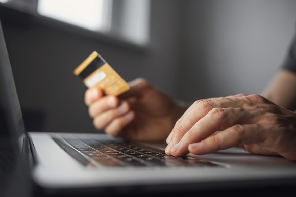 Person holding credit card in front of laptop.