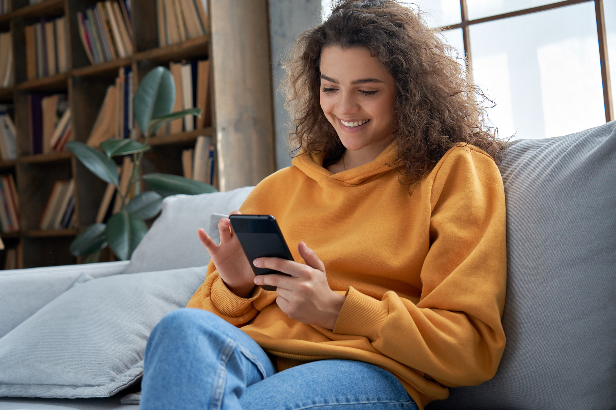 Person on couch smiling while using smartphone.
