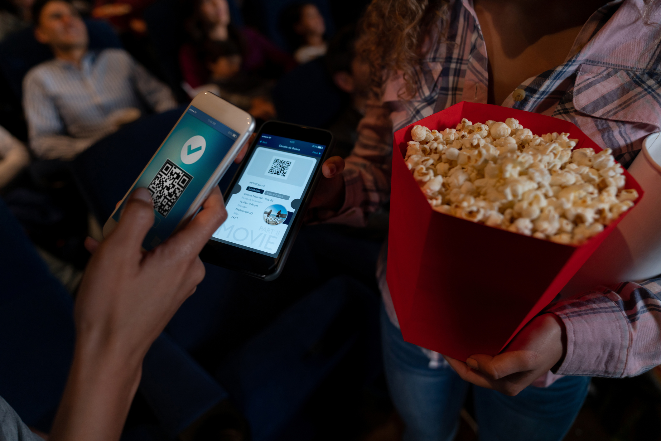 A popcorn-toting moviegoer shows a ticket code on a smartphone to an usher.