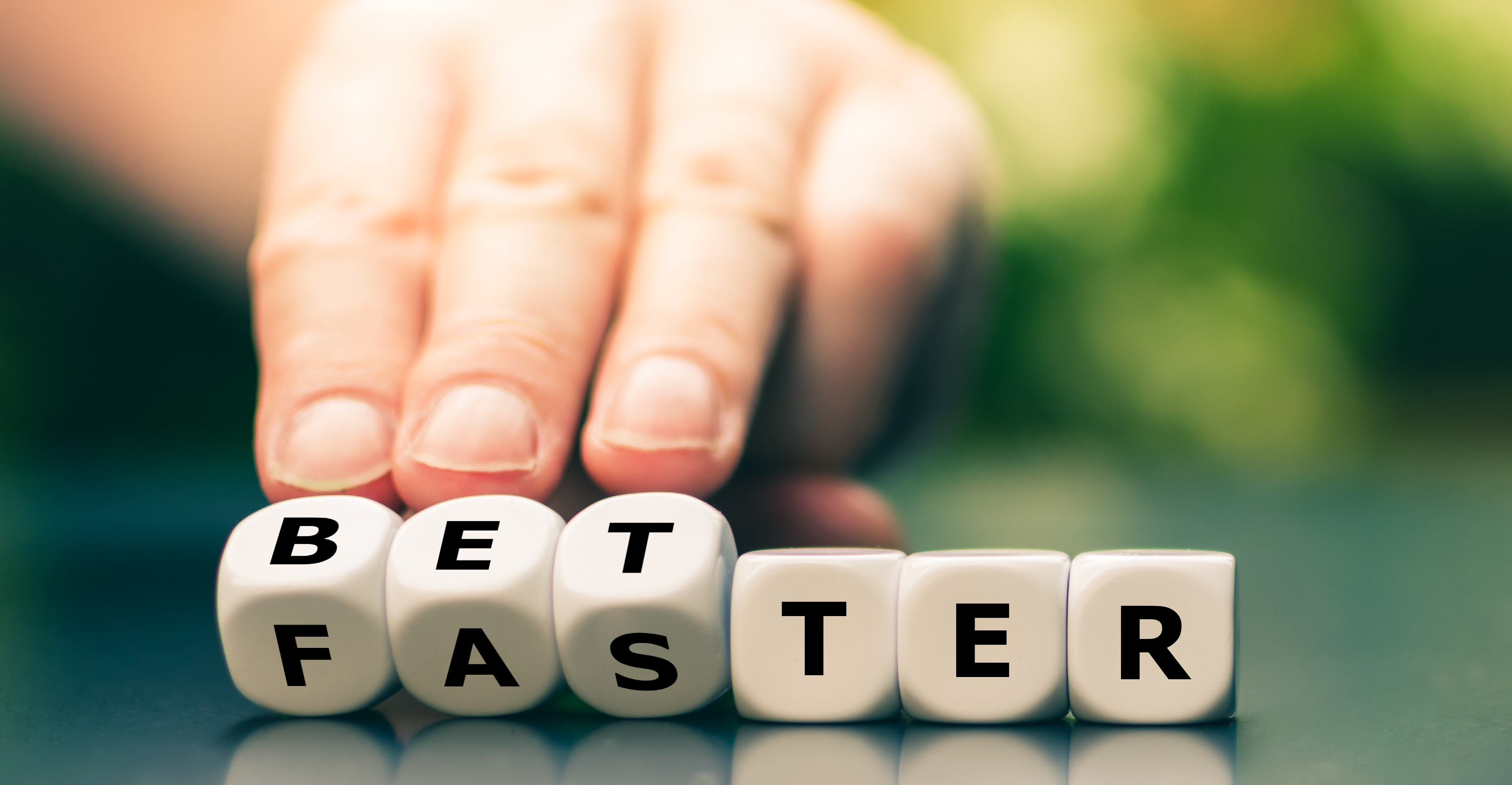 A person's hand turning dice spelling BETTER to FASTER.