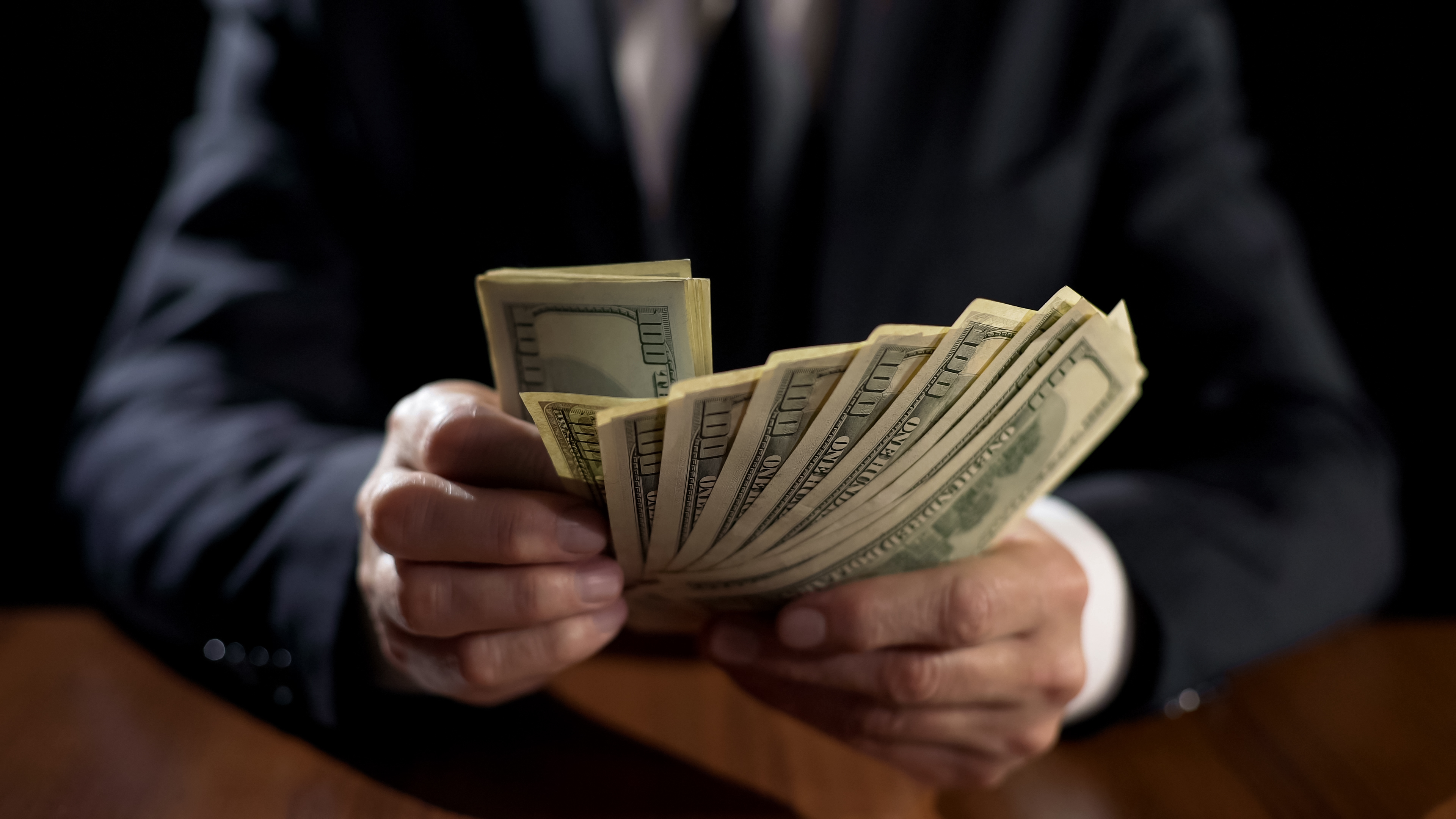 Business person holding a fan of hundred-dollar bills.