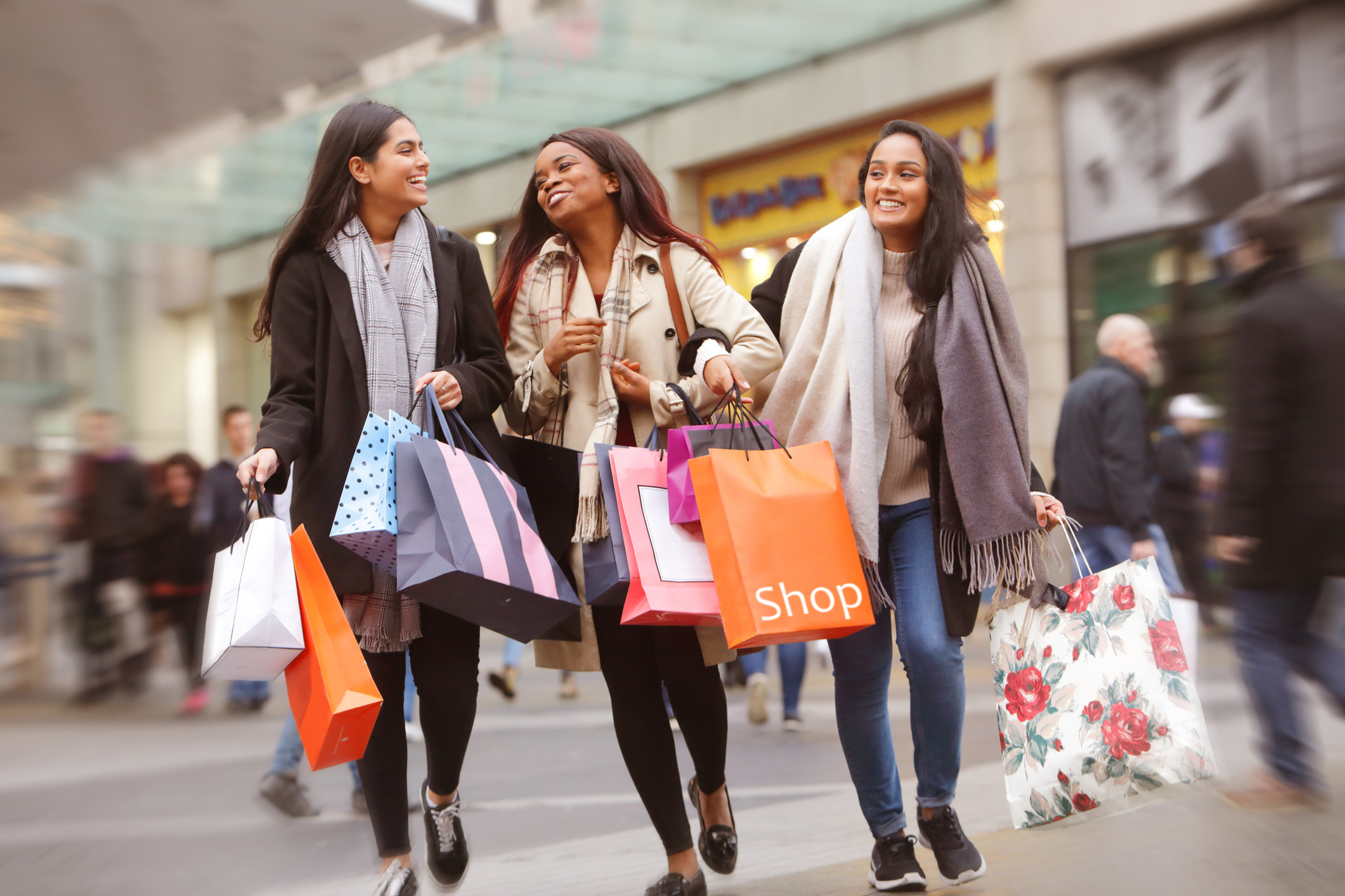 Three people walking through a mall holding shopping bags.
