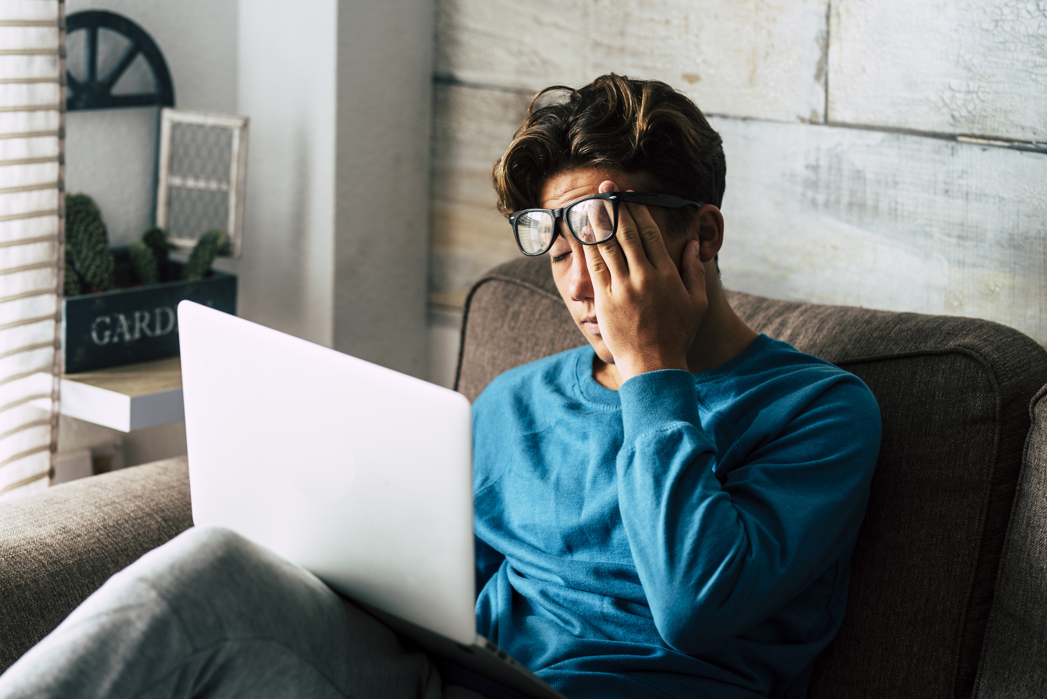 A person rubs their eyes while looking at a laptop.