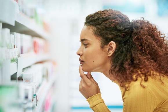 A shopper ponders bottles of medicine while standing in a pharmacy aisle.