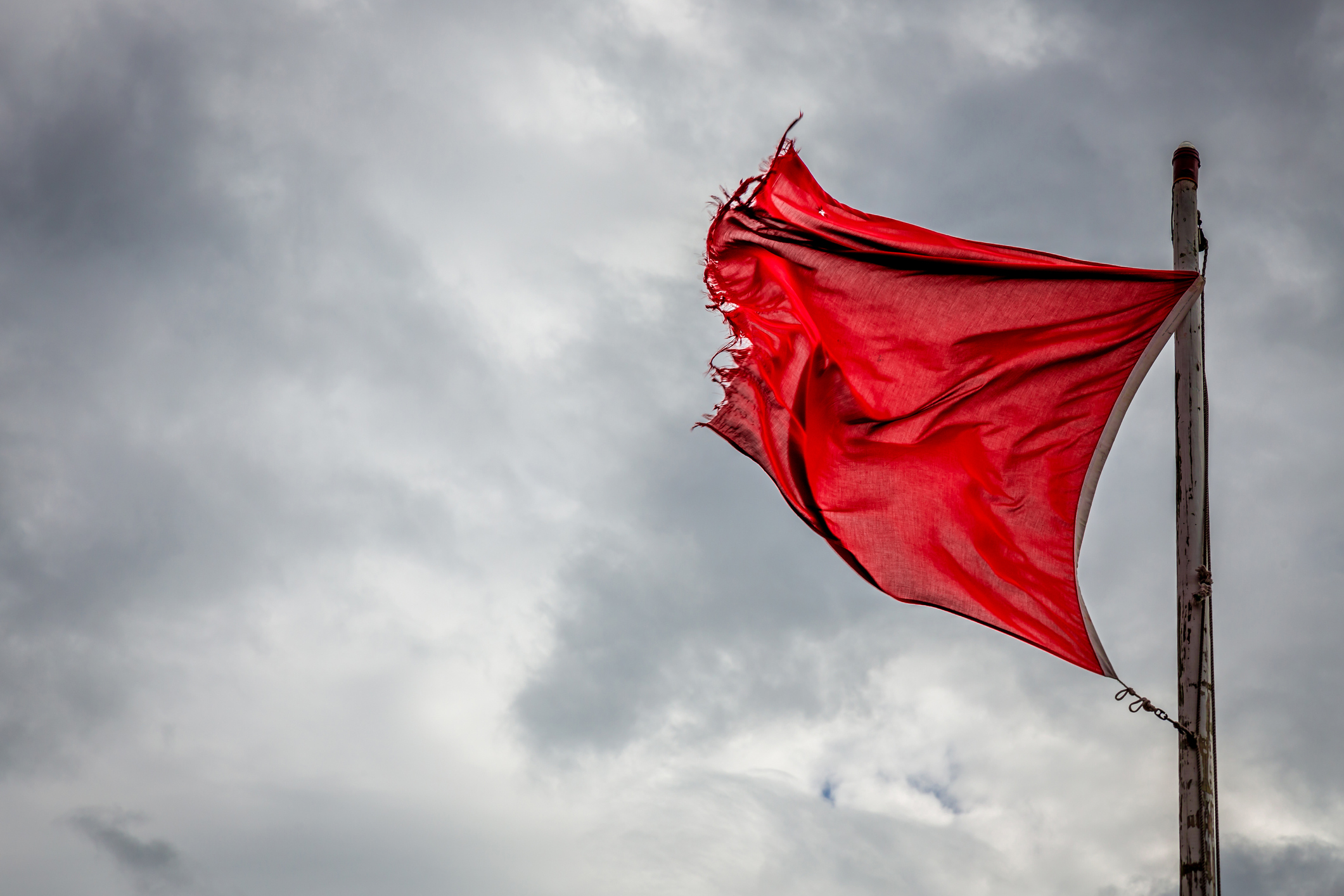 A red flag waving under gray, stormy skies.