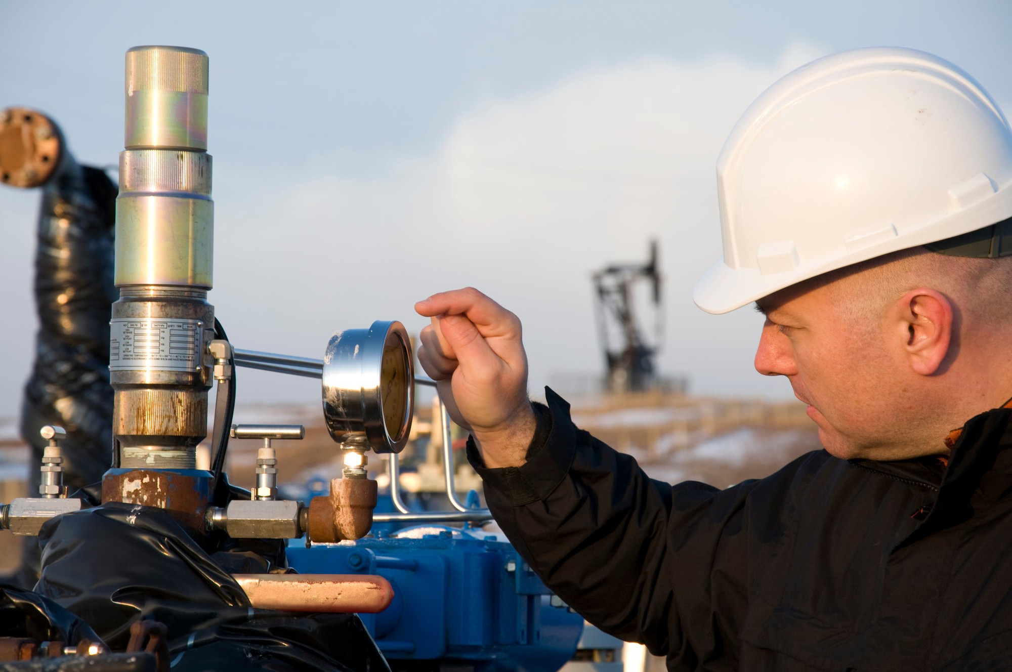 A man wearing a hardhat checks a gauge on a gas line.