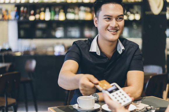 A person holding their credit card above a portable point-of-sale reader in a restaurant. 