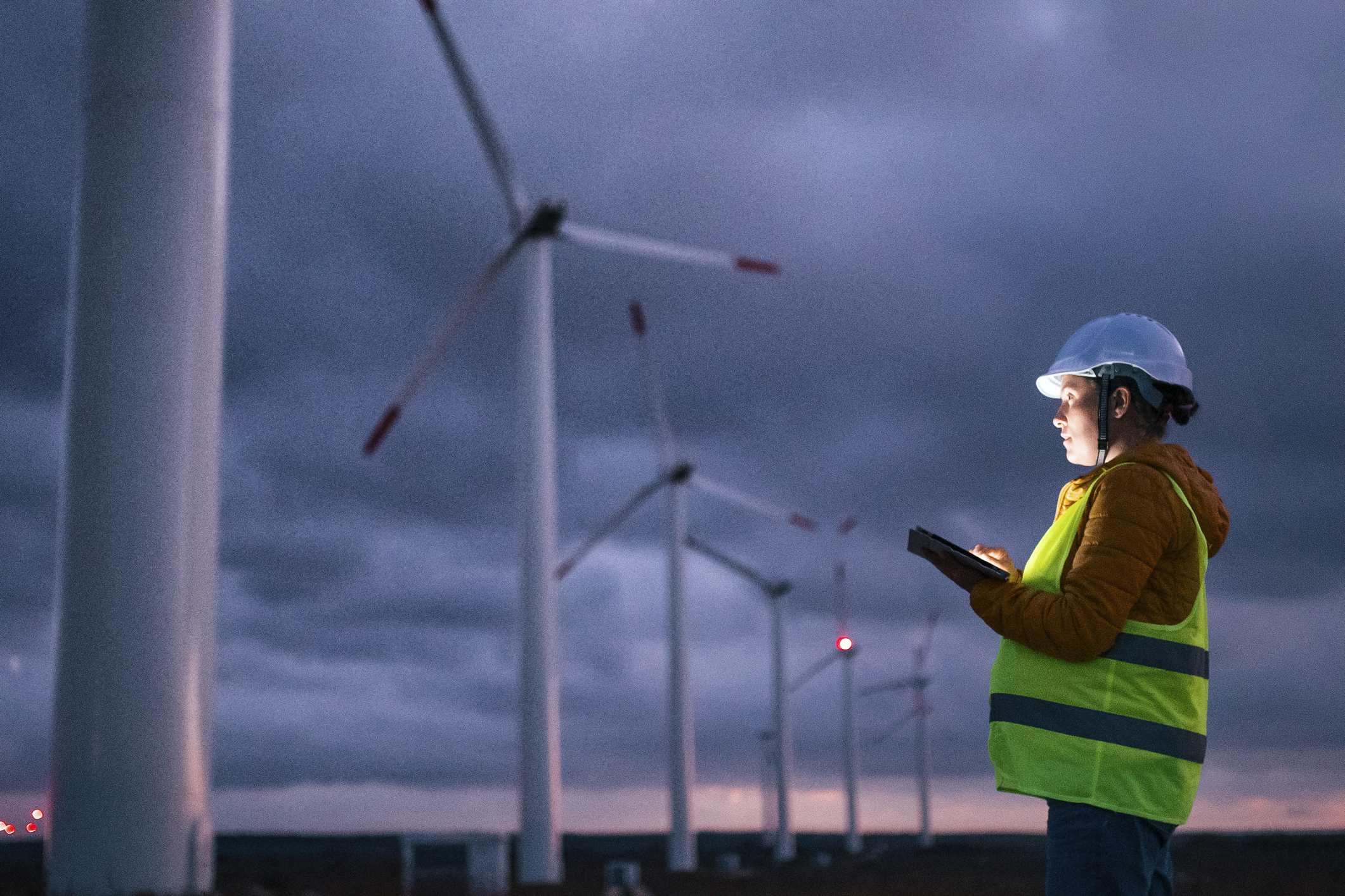 A person holding a tablet looking at wind turbines.