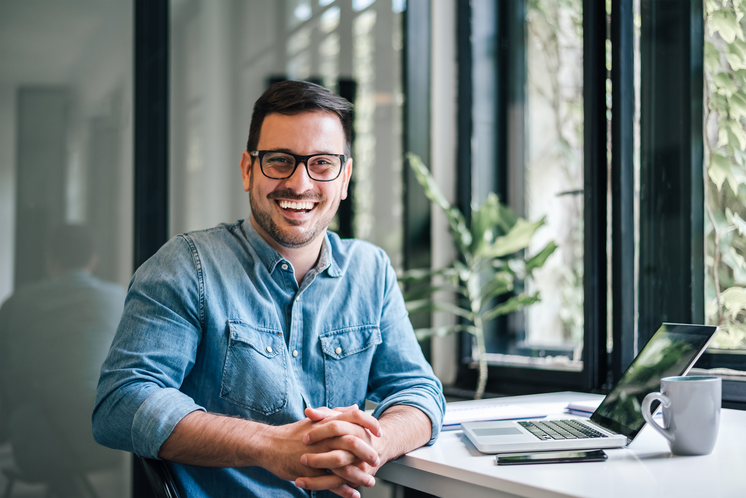 A smiling person at a table with an open laptop.