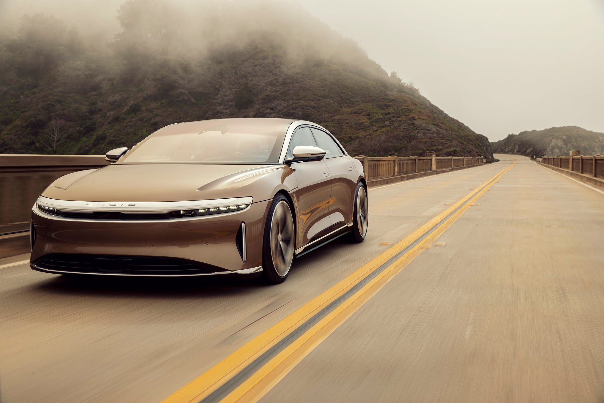 A brown Lucid Air electric sedan cruises down an open road.