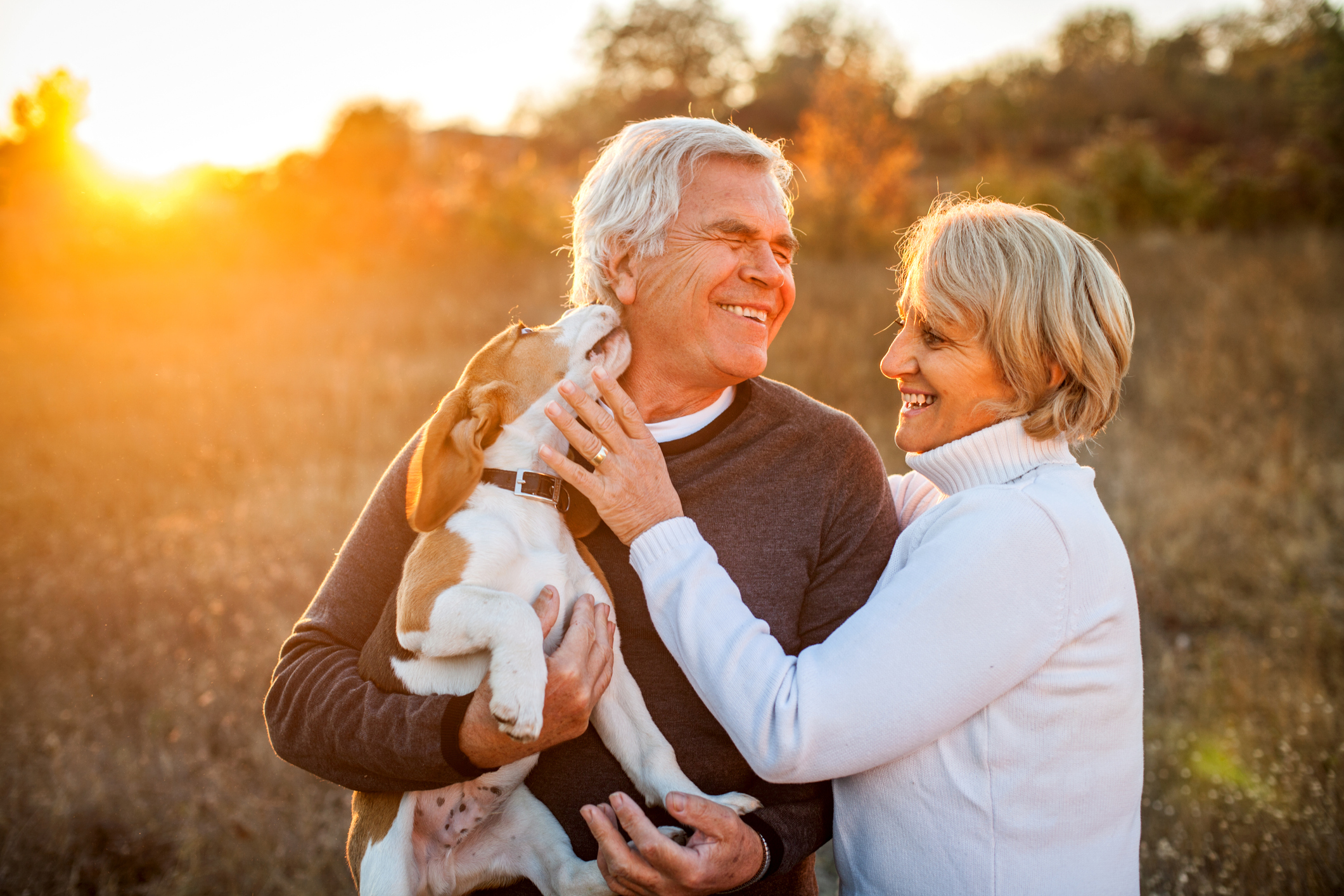 Two people holding and petting a dog outside.