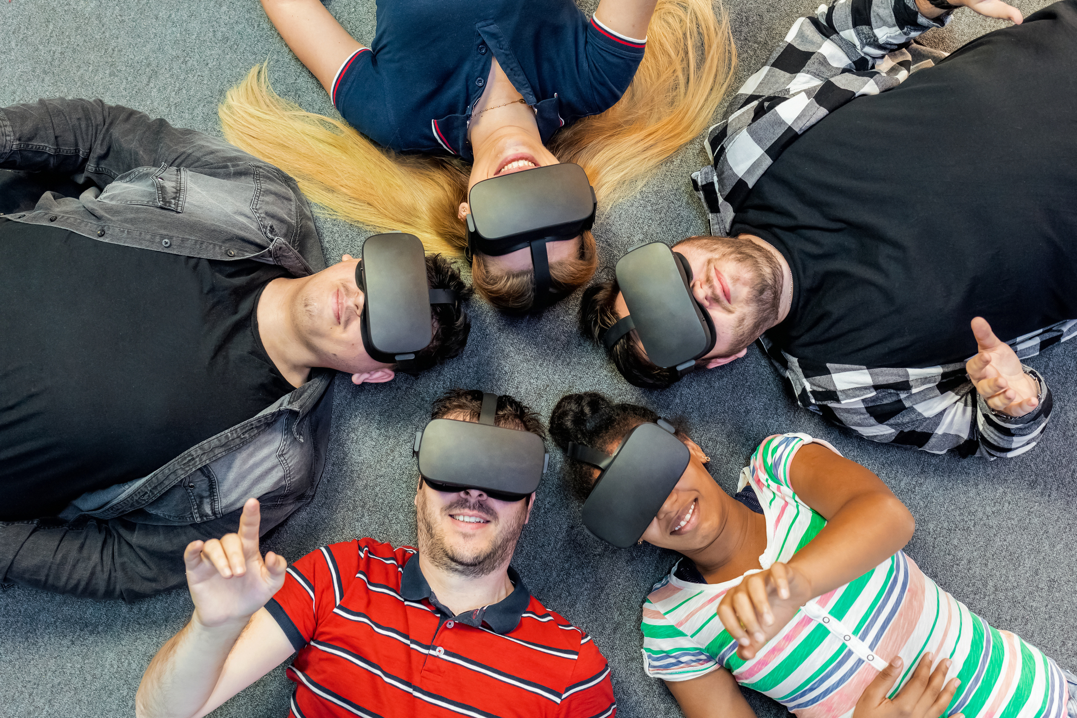 Five people wearing virtual reality headsets lie in a circle on the ground.