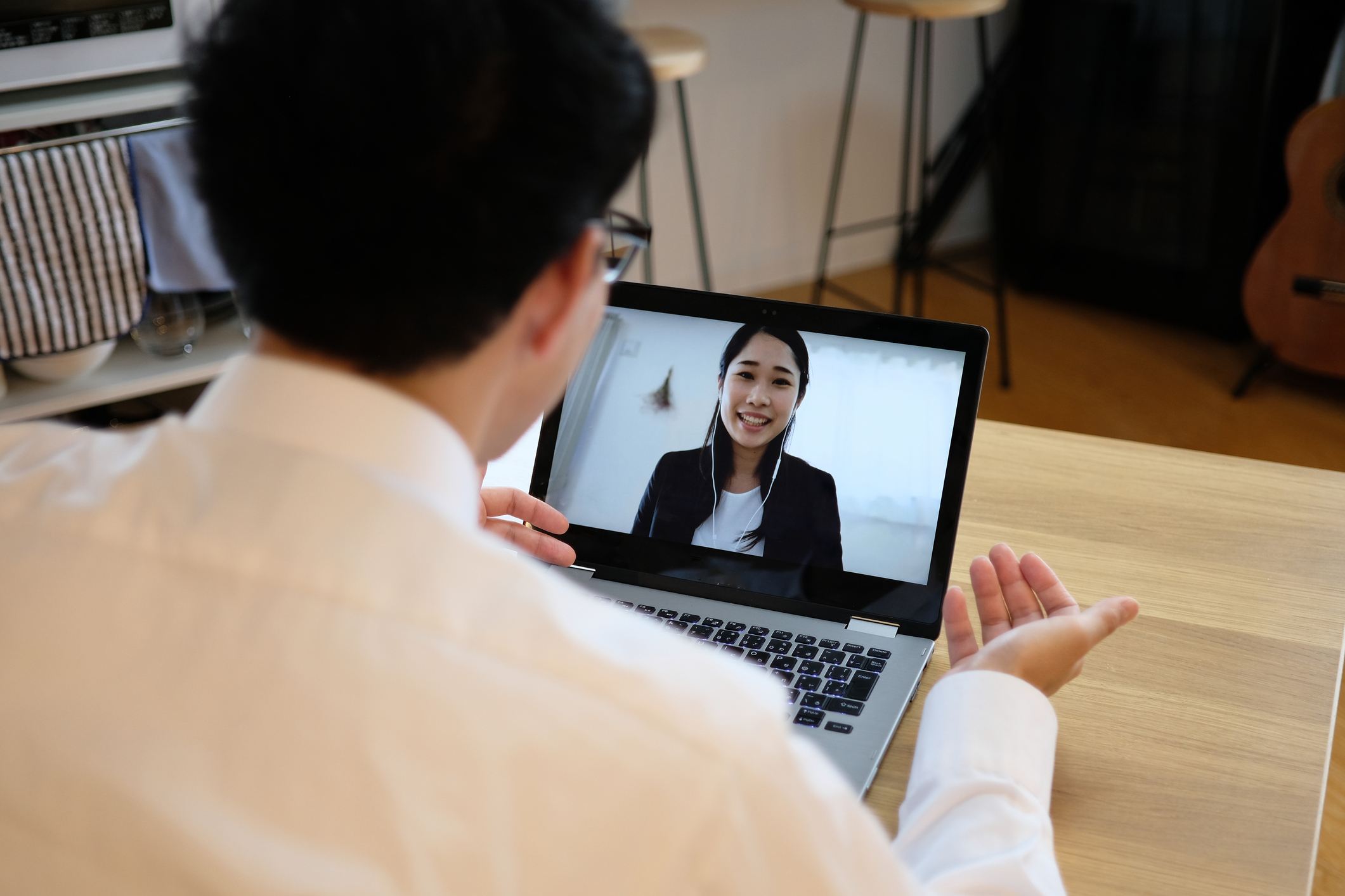 Person seated at a table dressed in business attire, having a discussion with another person via laptop.