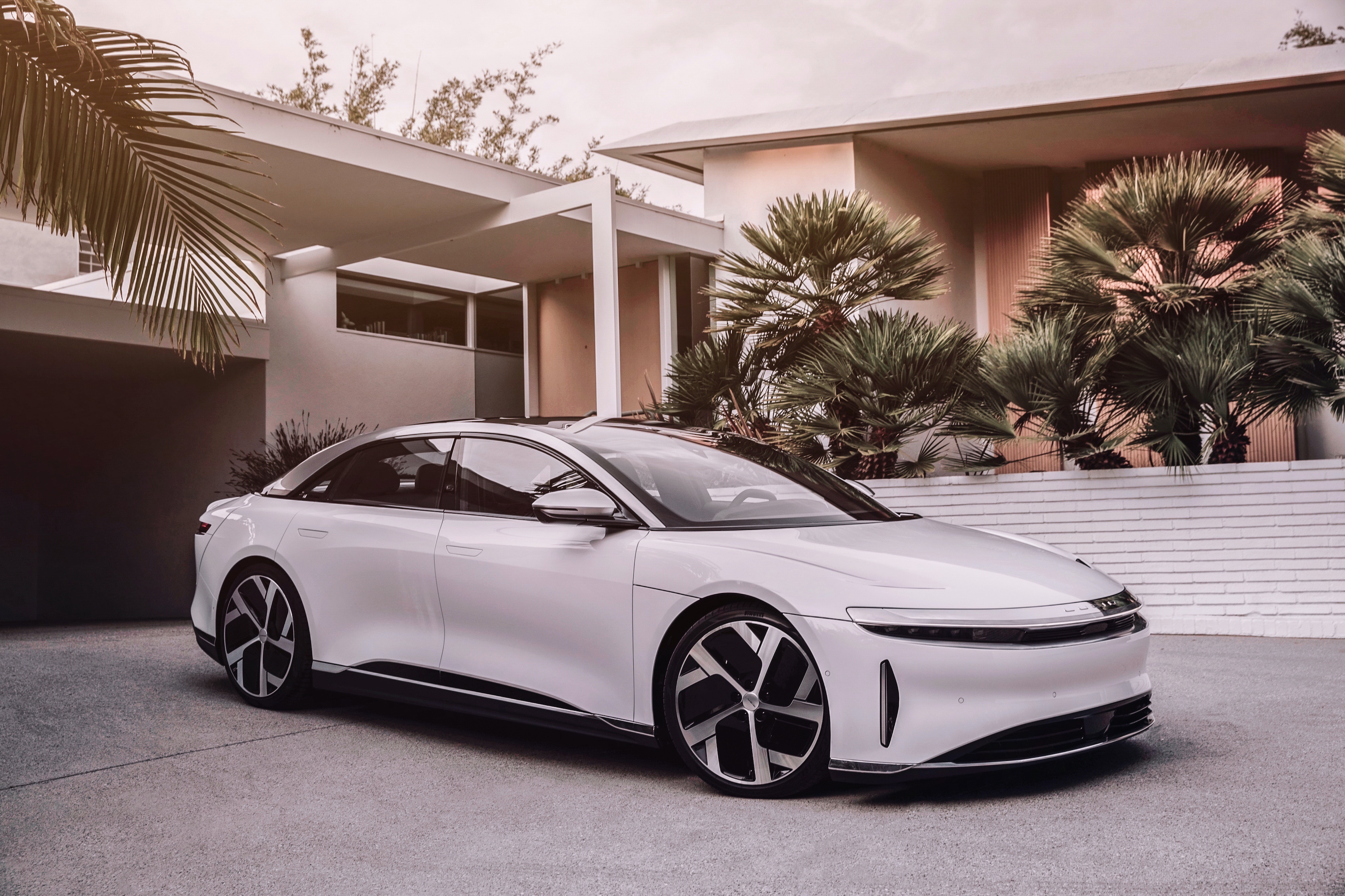 A white Lucid Air electric sedan parked in front of a building with palm trees.