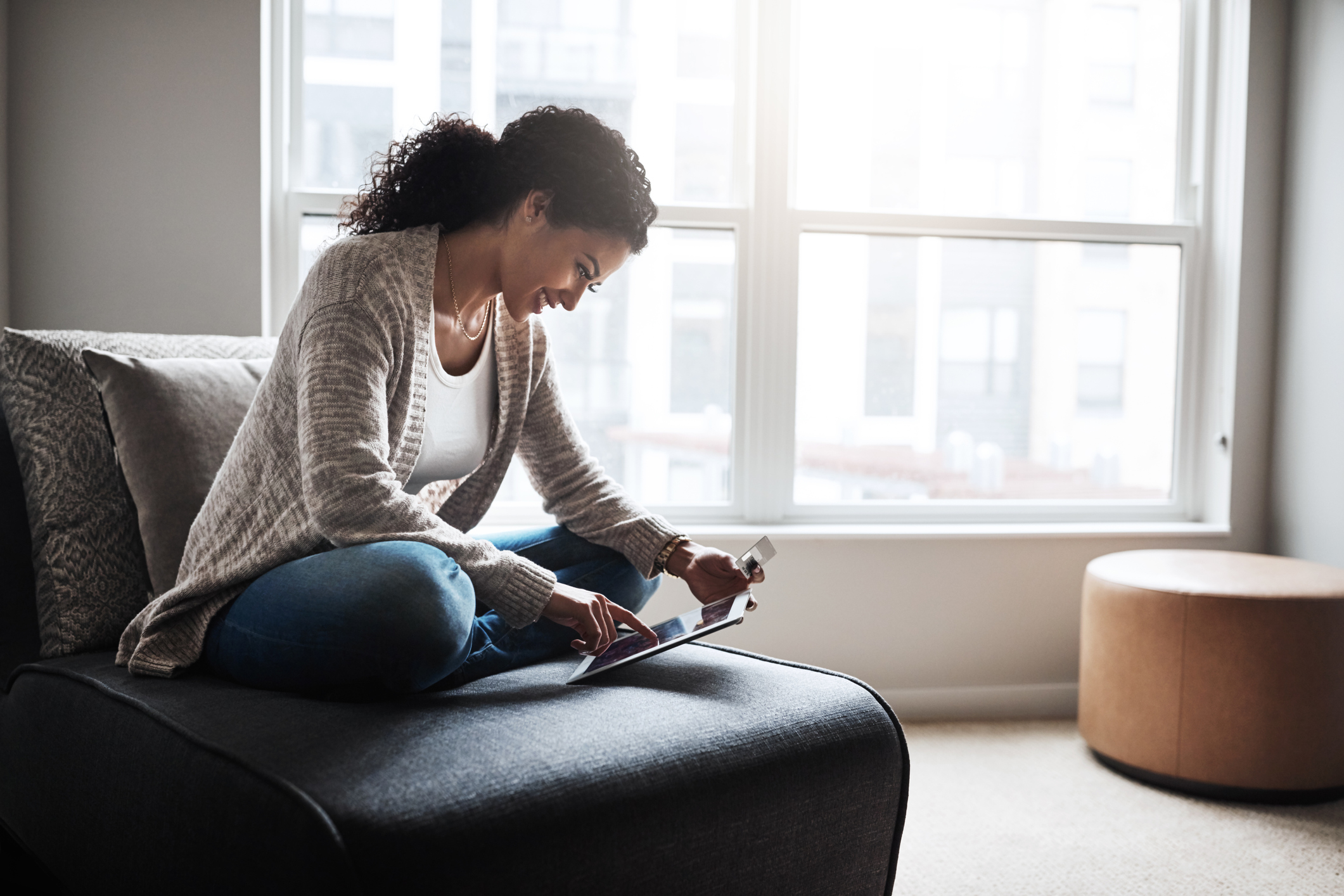 A woman sits on a chair while working on a tablet.