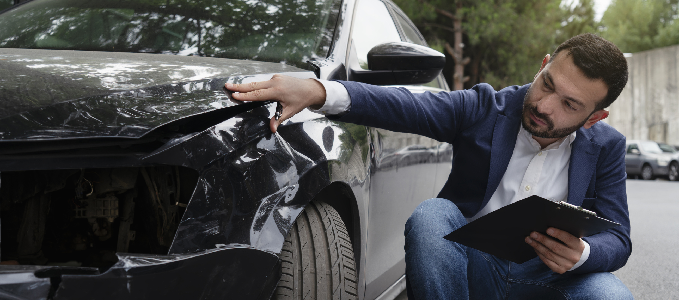 A man with a clipboard reviews damage to a car.