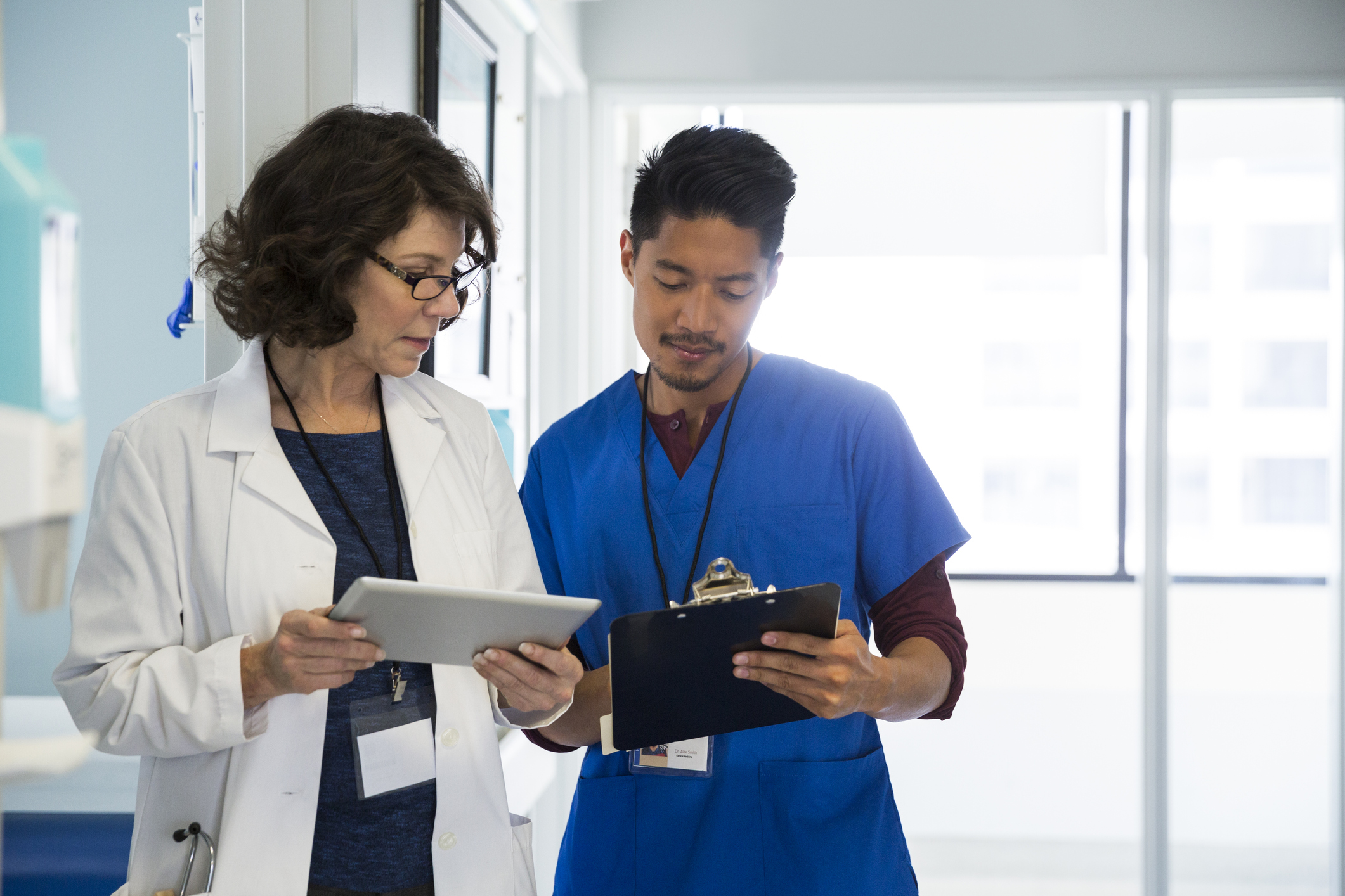 Two healthcare workers looking at a tablet and a clipboard.