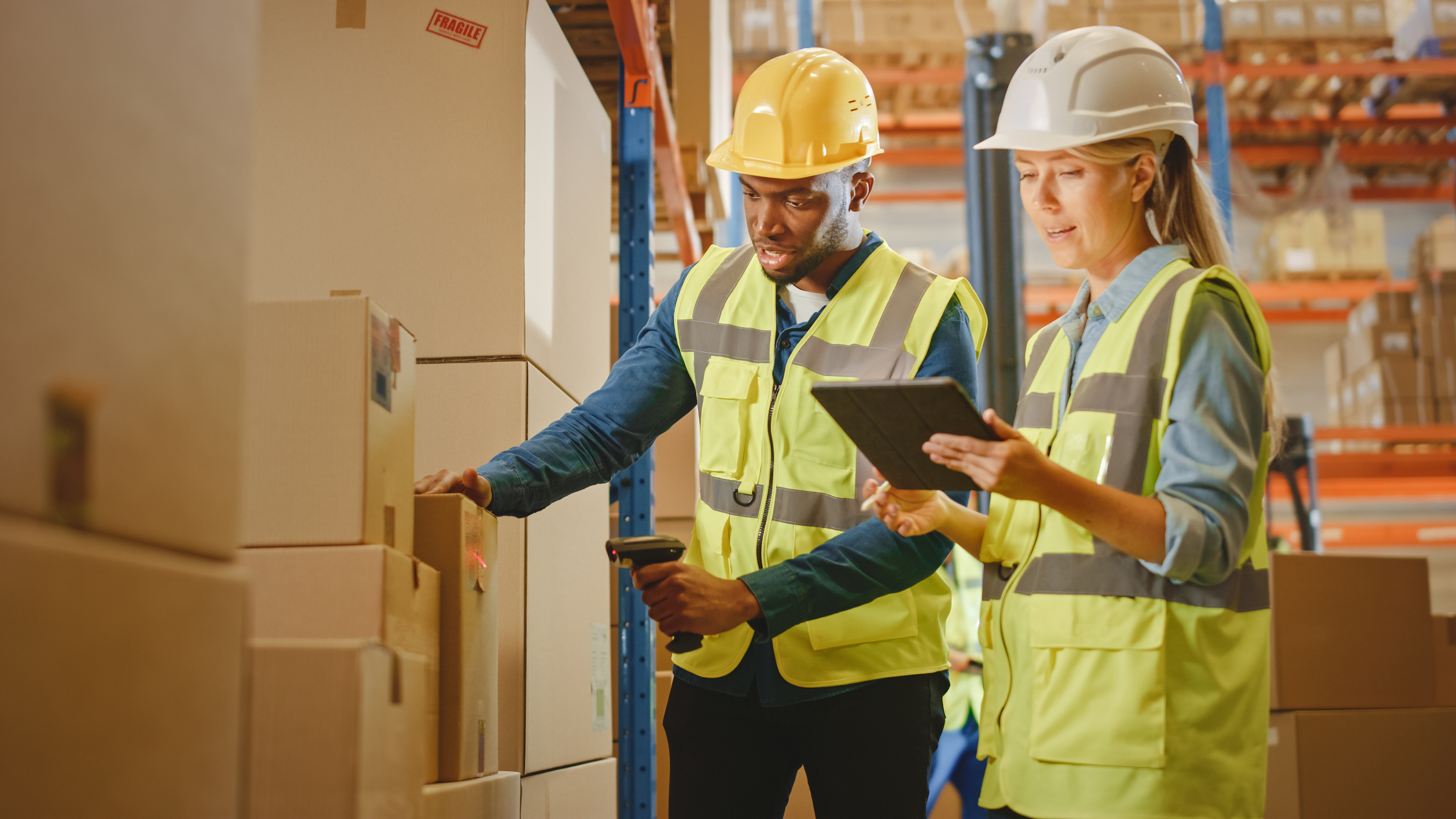 Two people in hardhats and yellow vests with a barcode scanner and tablet.
