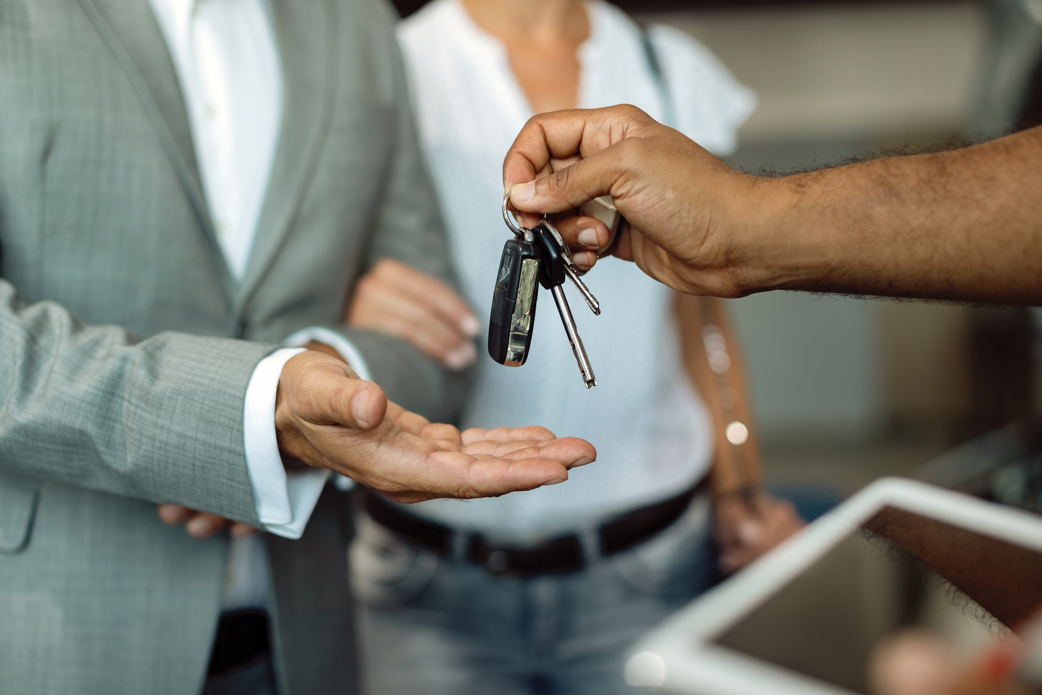 A hand is giving car keys to a couple.