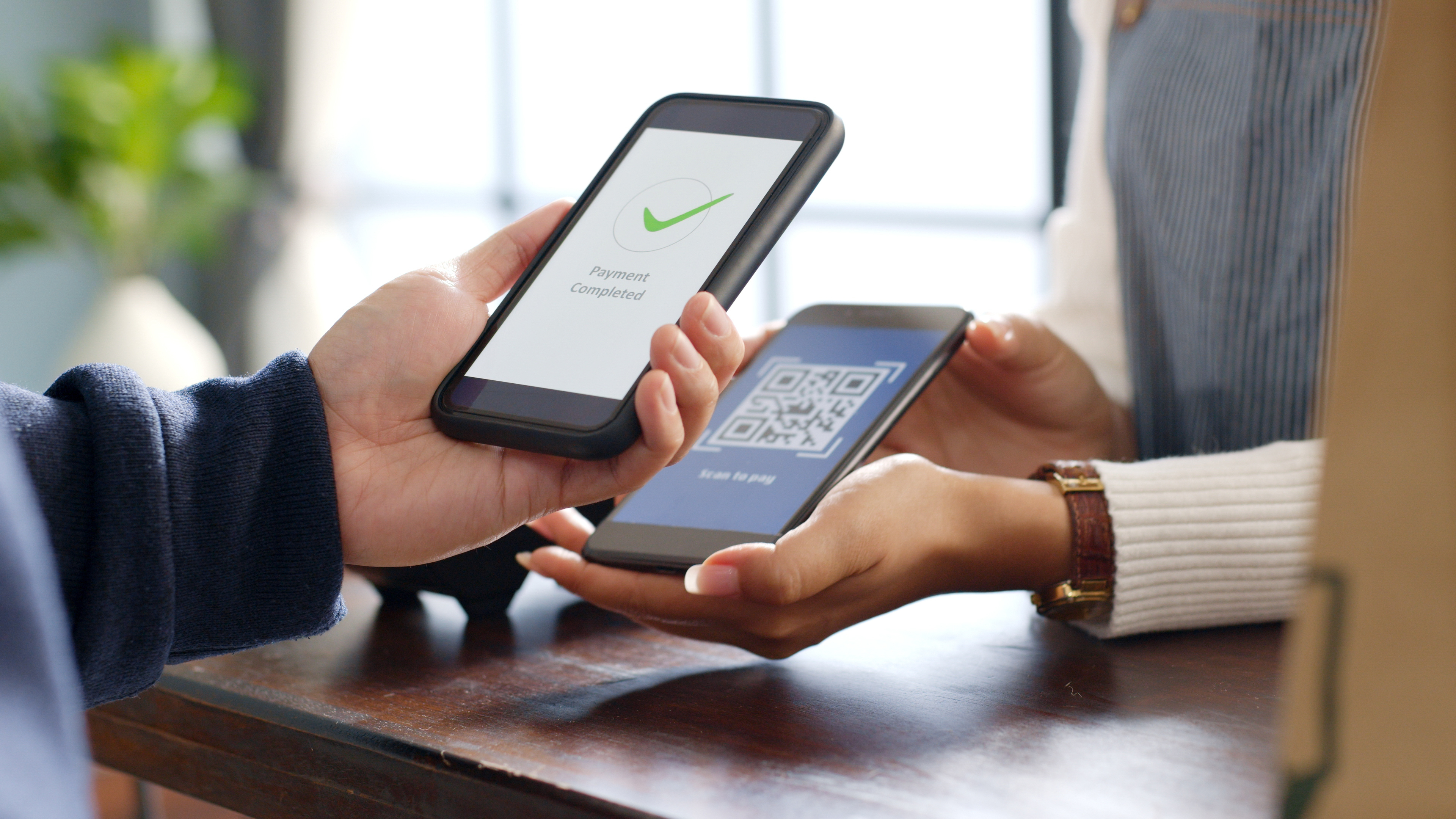A person holds a phone showing a confirmation page over another phone showing a QR code to make a contactless payment.