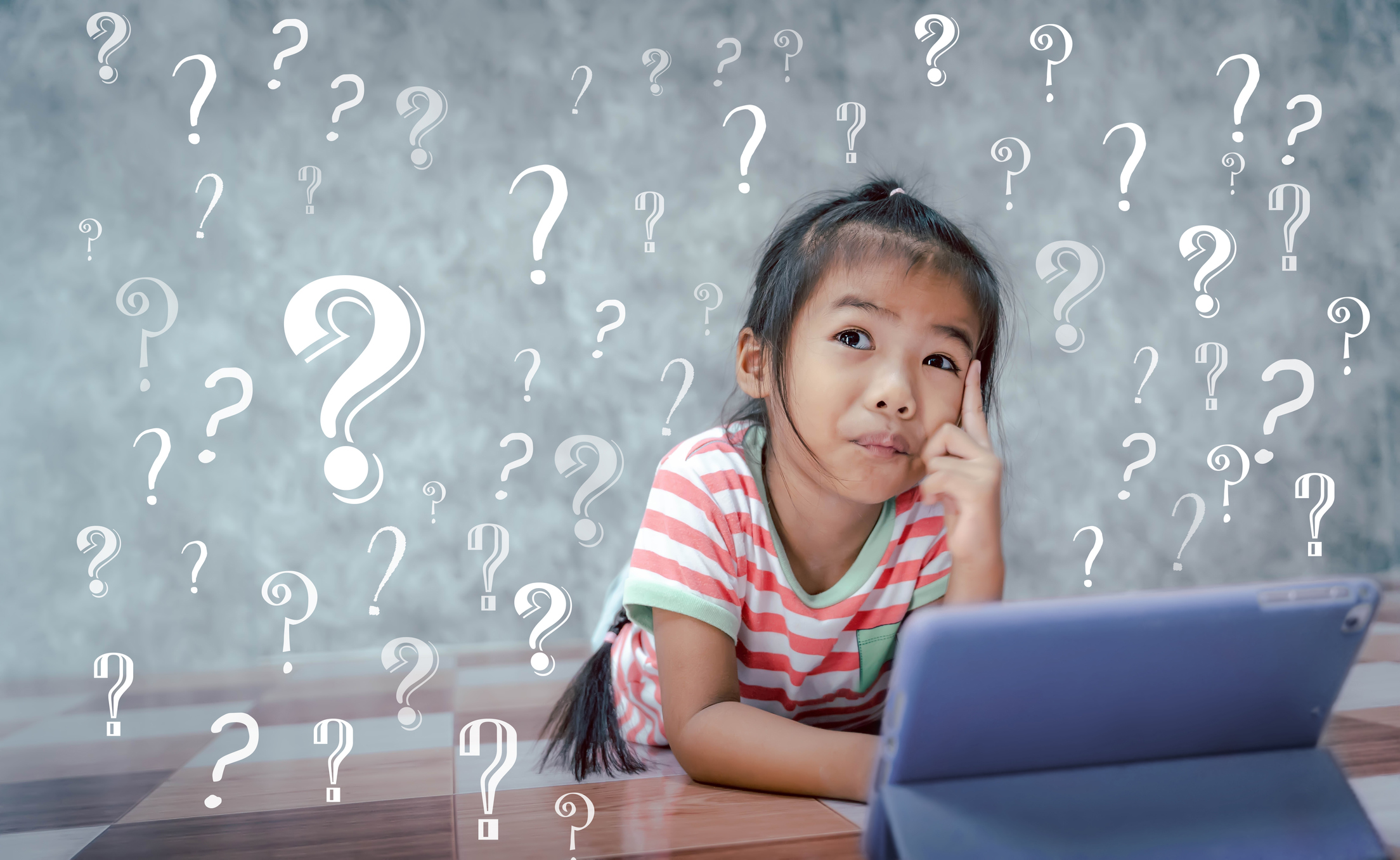 Question marks surround a girl who is working on a tablet.