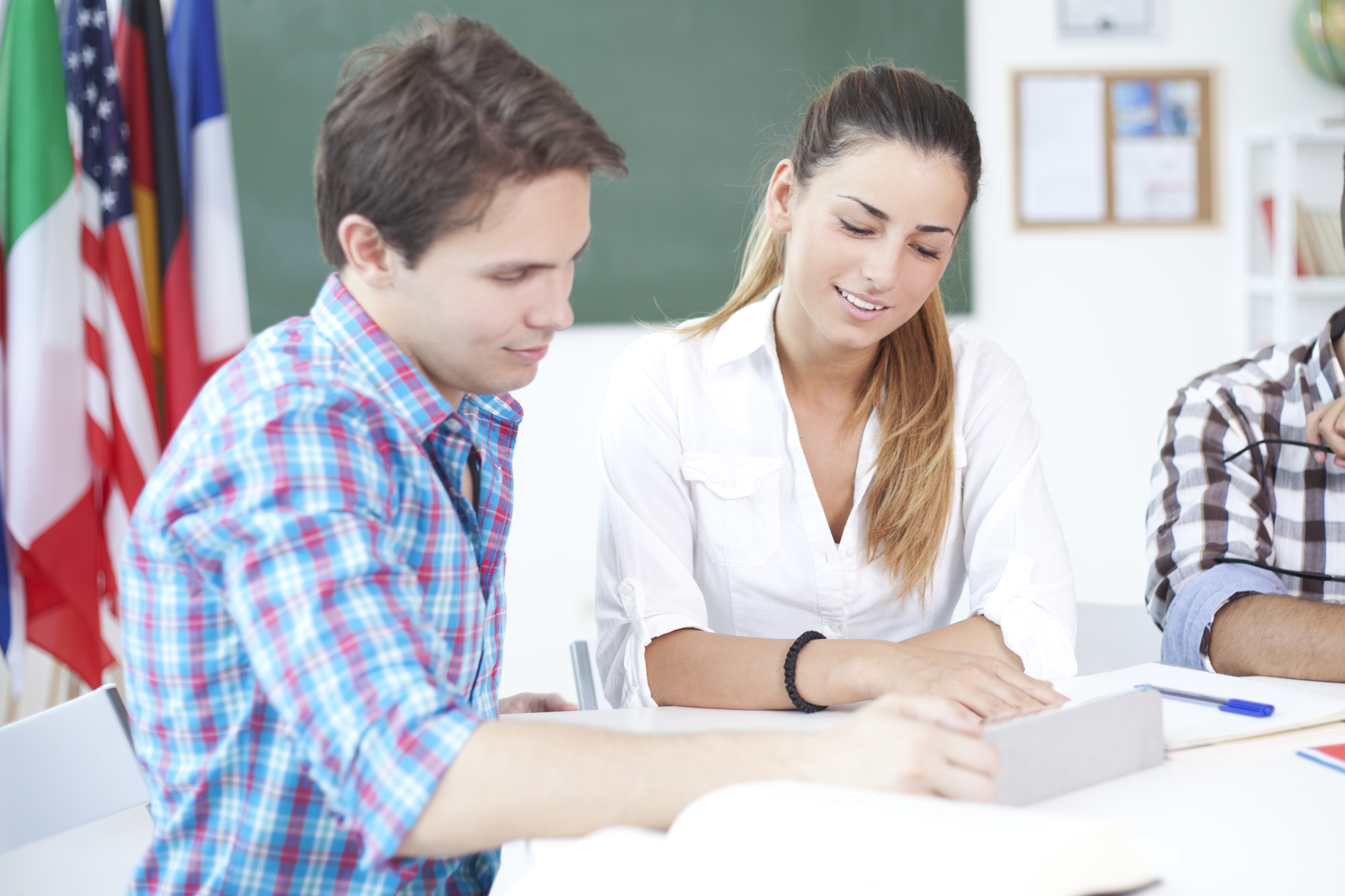 Two students sitting at a table studying, with several countries' flags in the background.