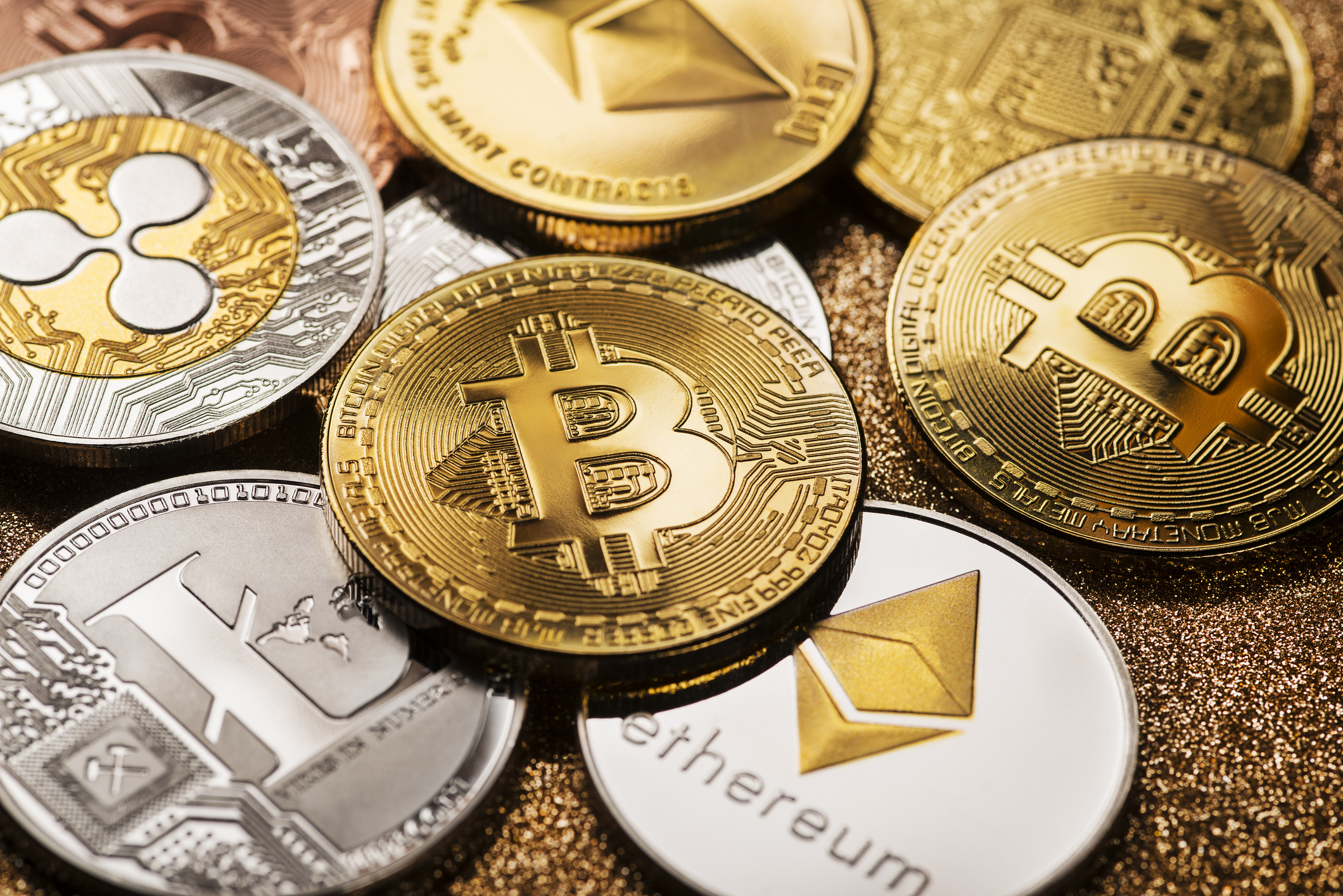 A loose pile of gold and silver coins, stamped with various cryptocurrency logos.