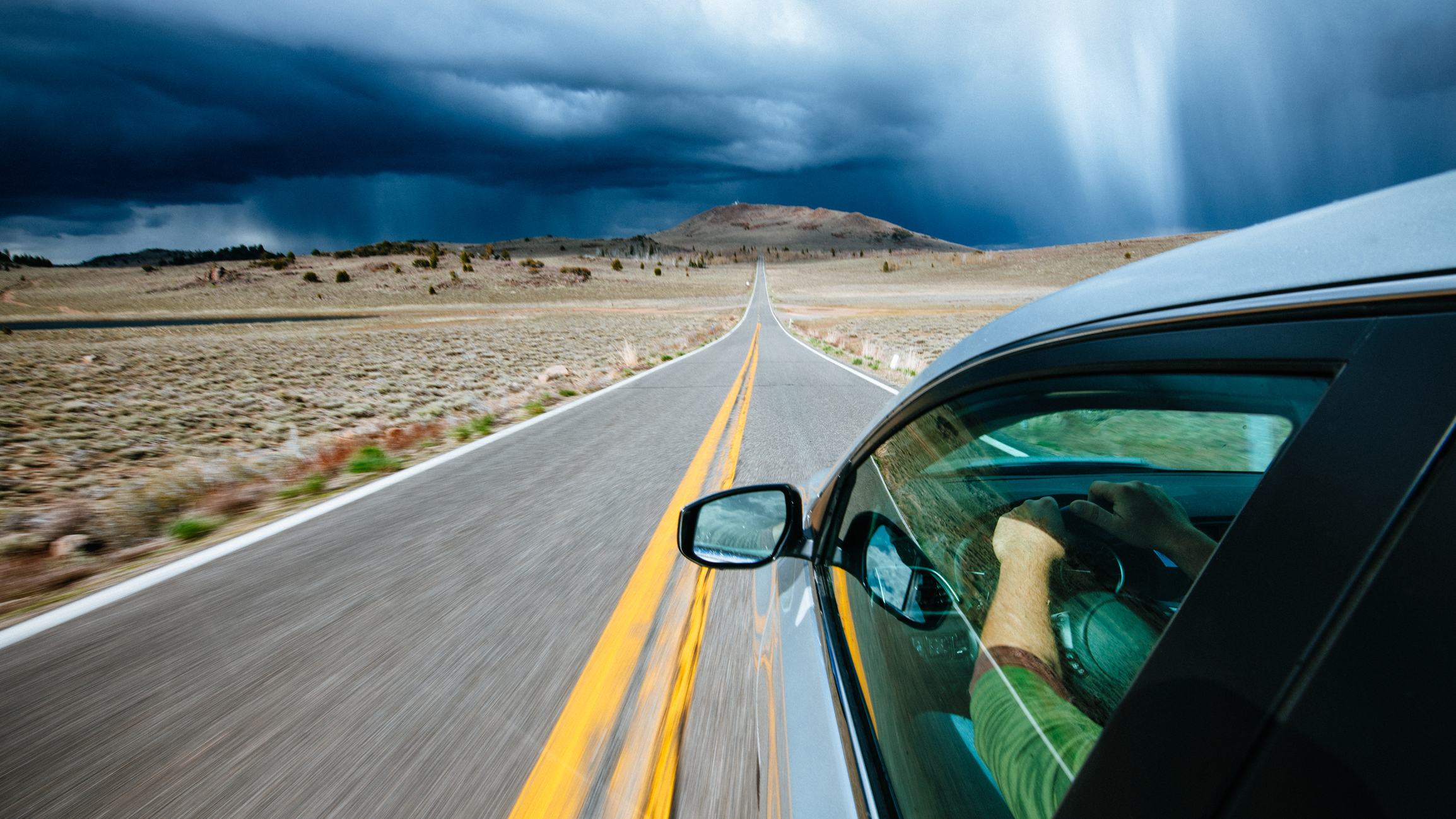 Car driving down a long road toward a hill in the distance.