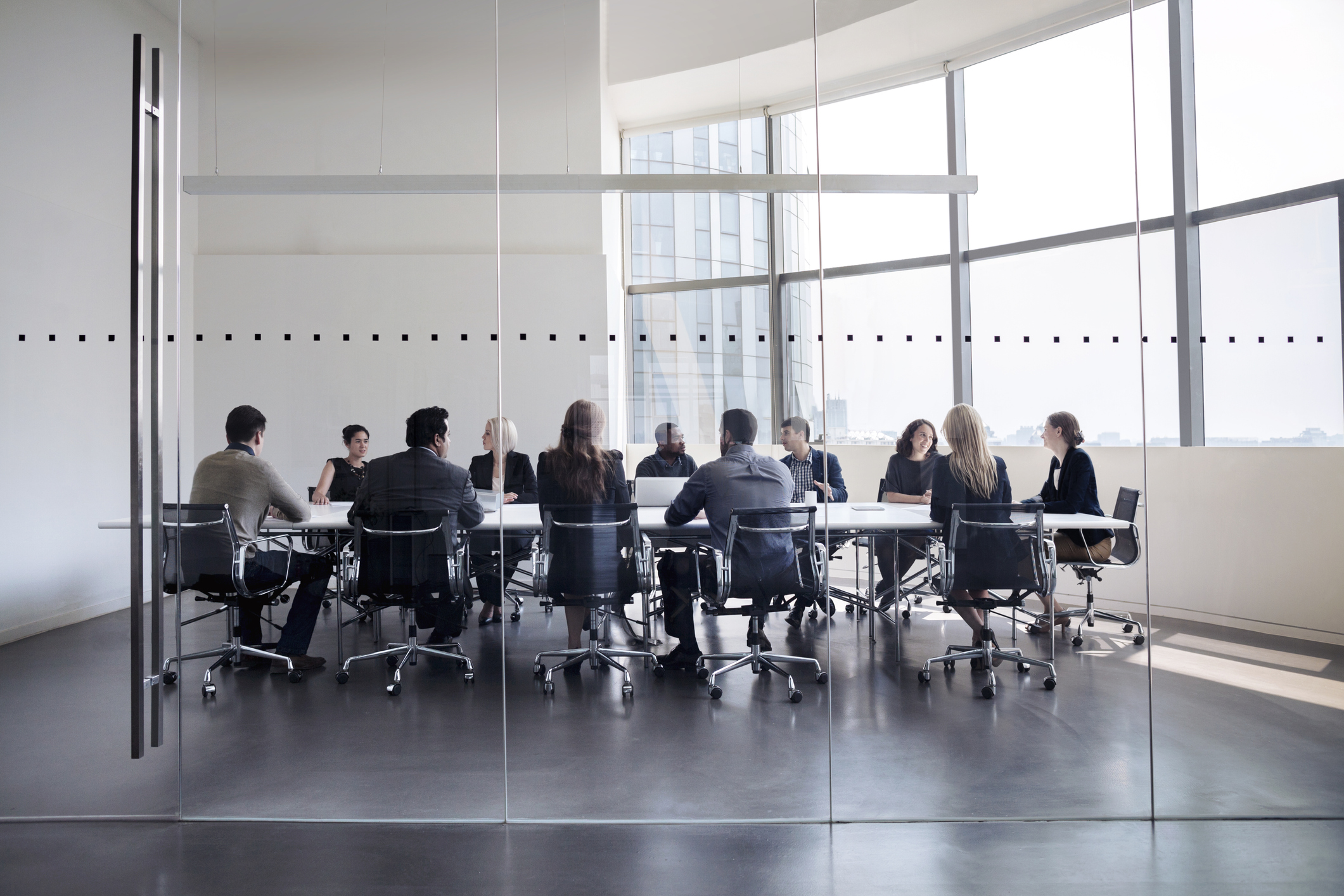 Professionally-dressed executives having a meeting around a table in a glass-walled conference room