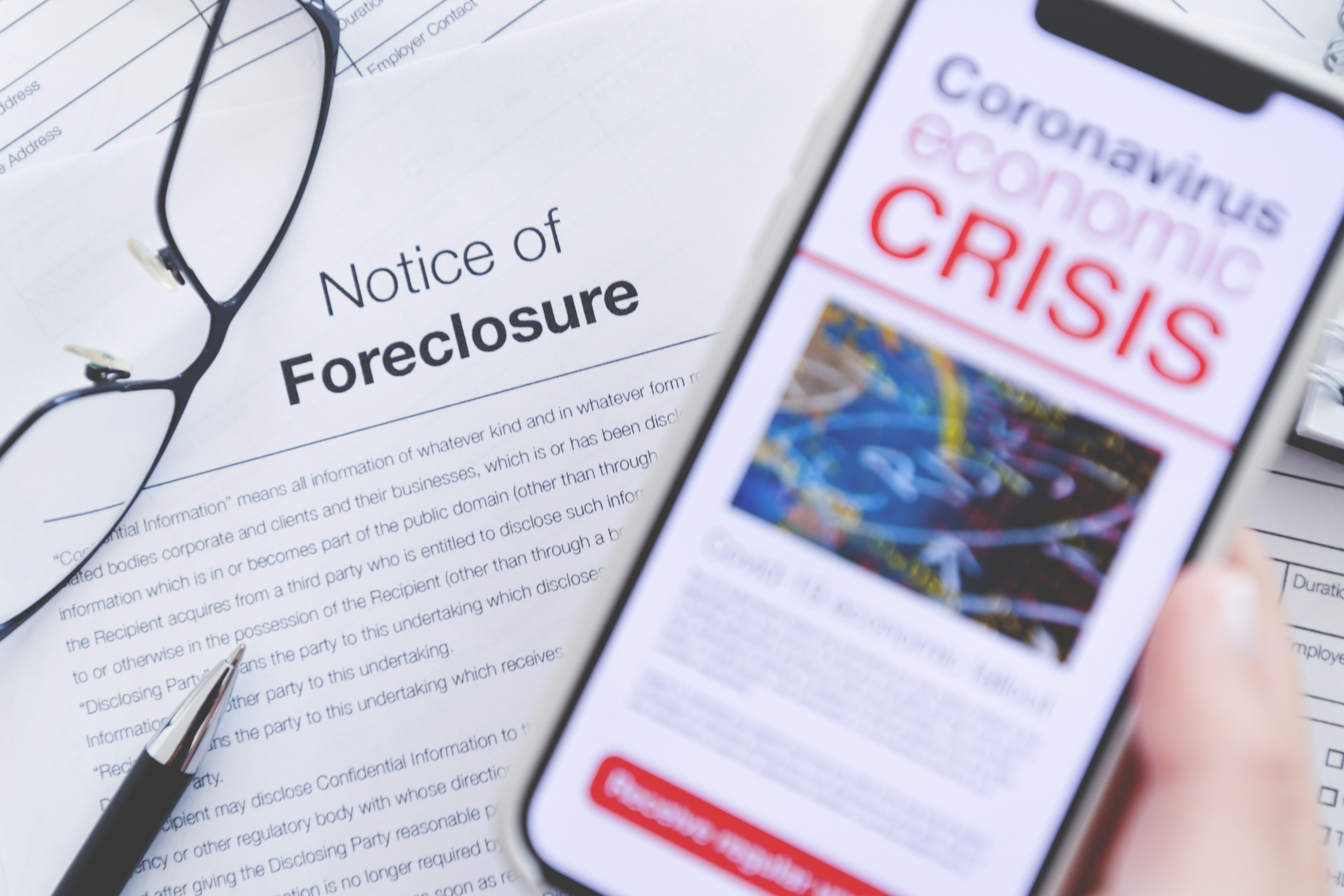 Person holding phone with words economic crisis over notice of foreclosure paperwork.
