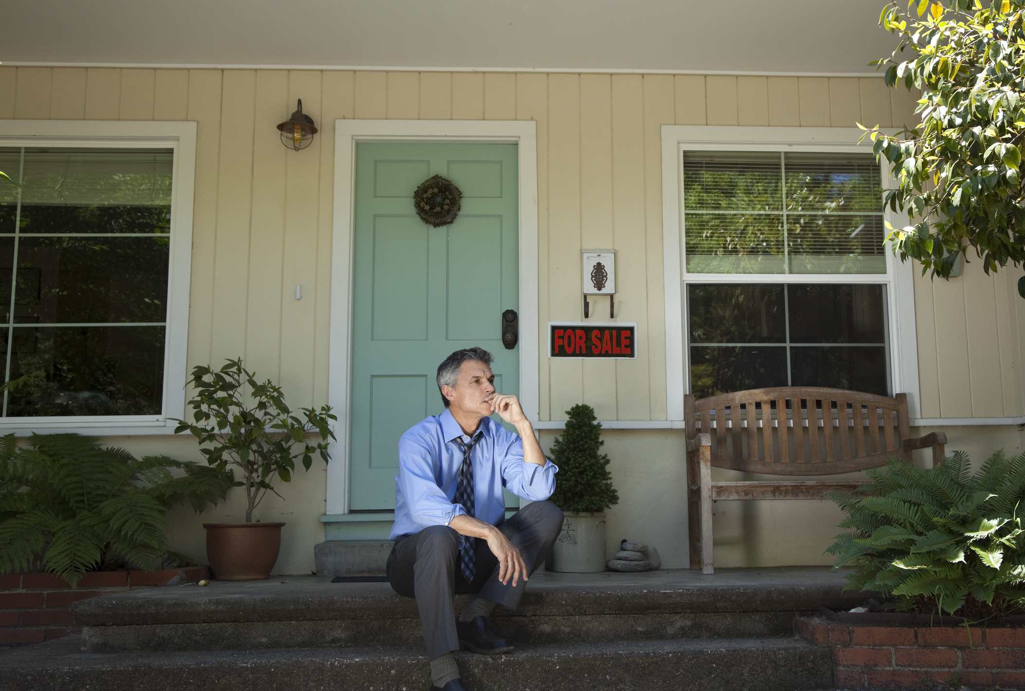 Person sitting on front porch with for sale sign looking worried.