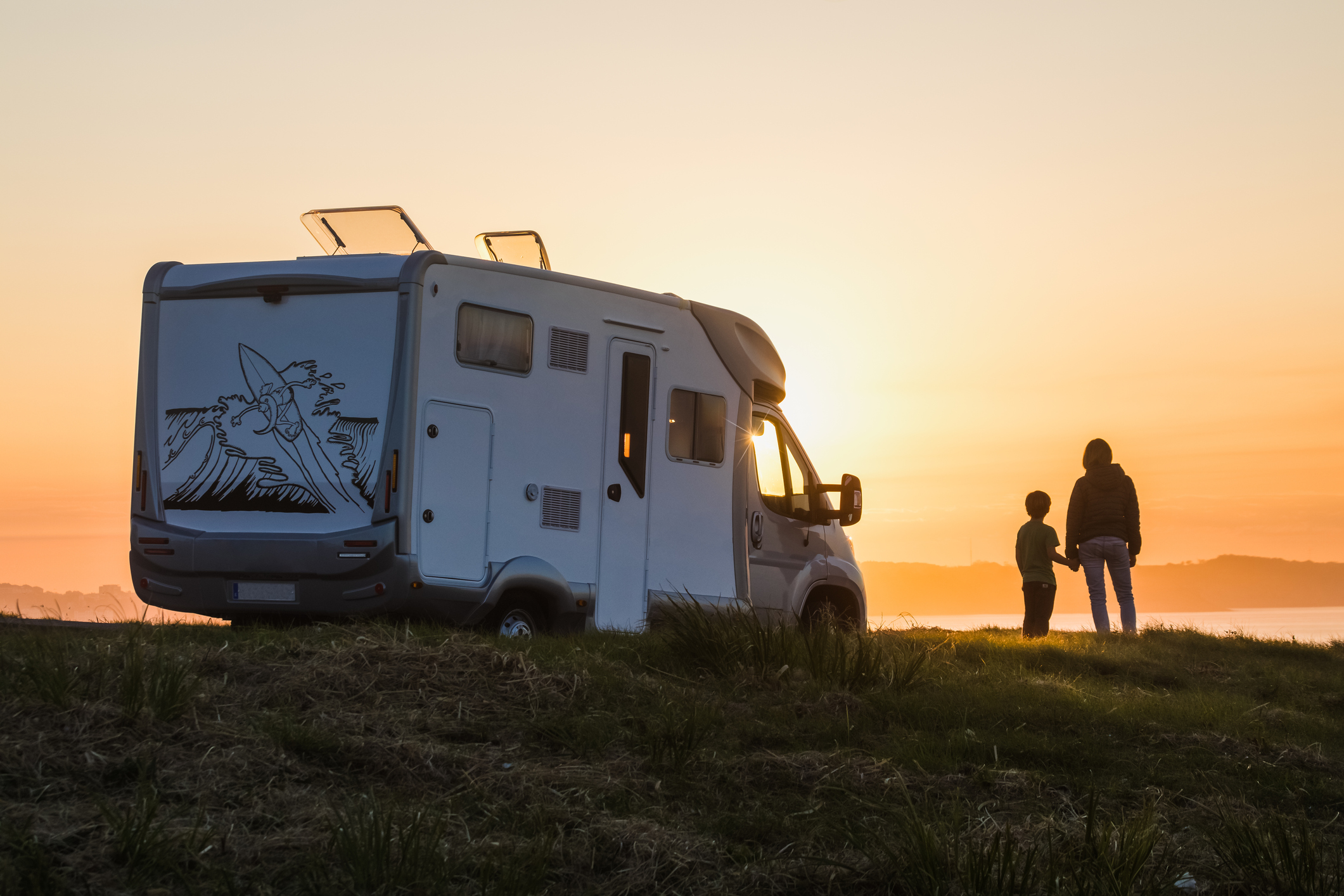 RV parked on a ridge with an adult and a child watching the sun set.