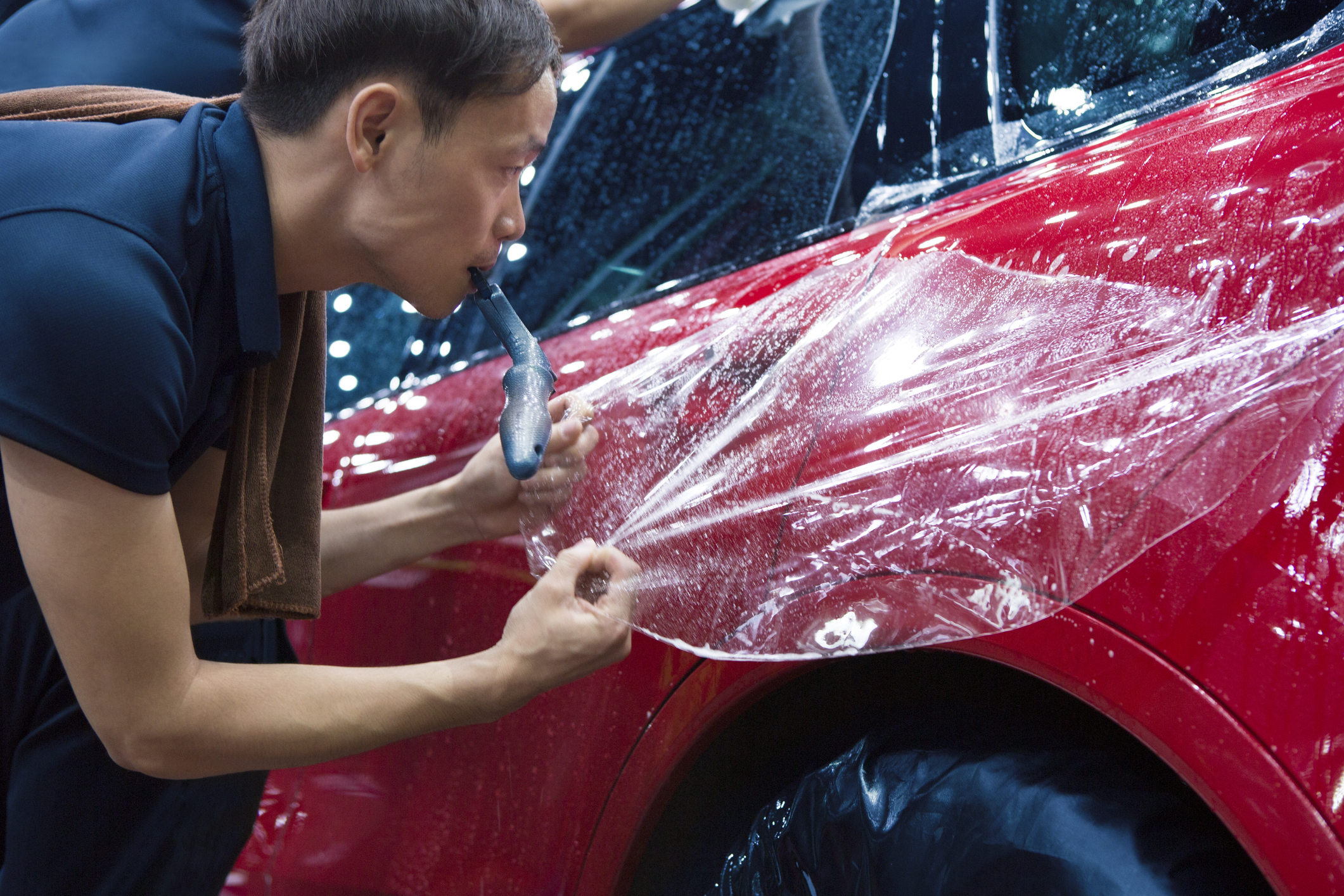 A person of Asian ethinicity working on a car at a workshop.