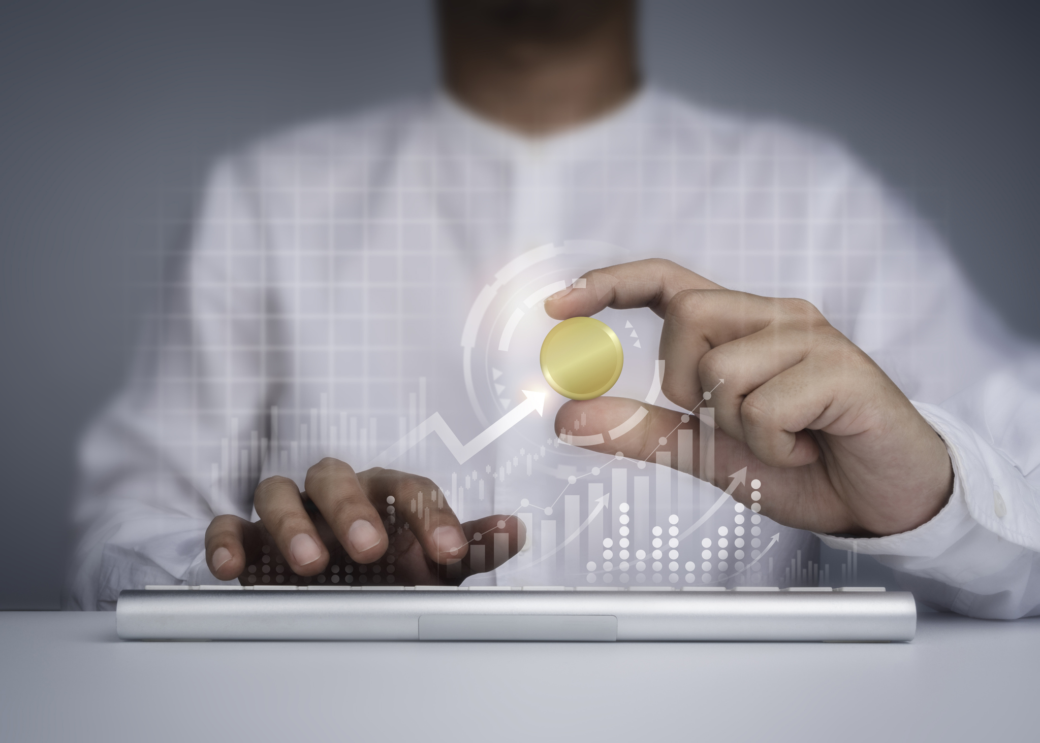 A person holding a gold coin above a keyboard.