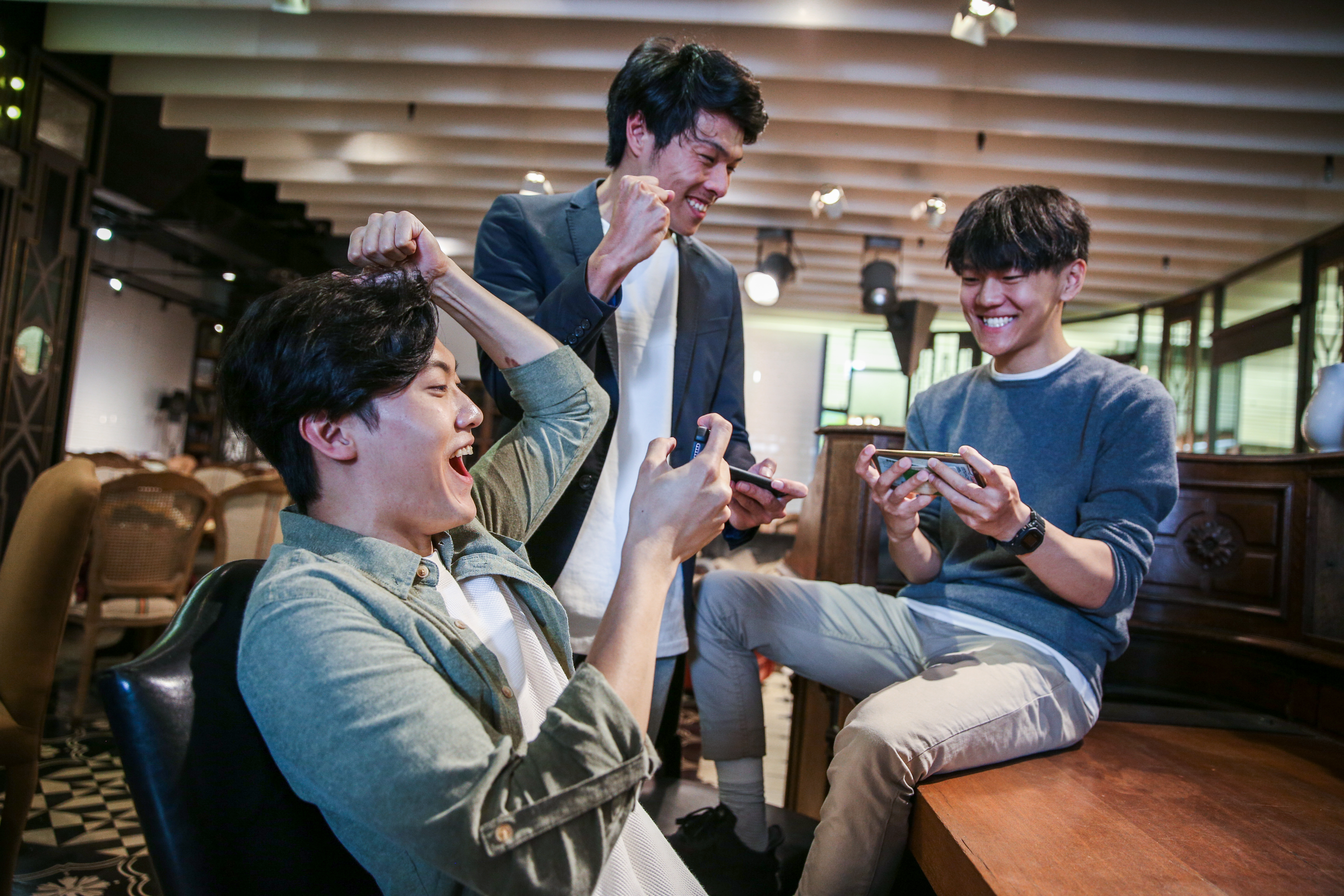 Three smiling friends playing mobile games and celebrating.