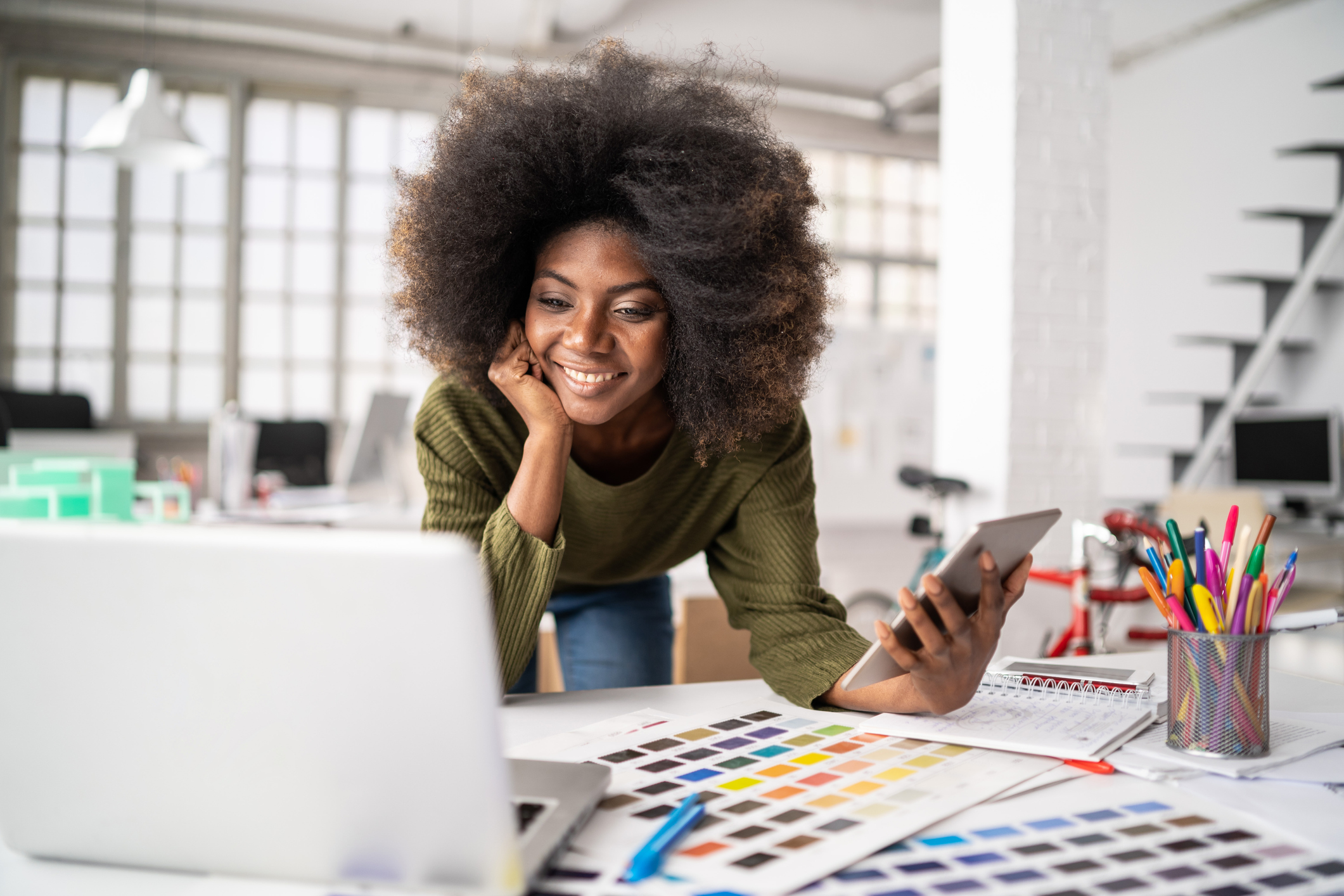 A person holds a tablet and looks at a laptop in a studio office.