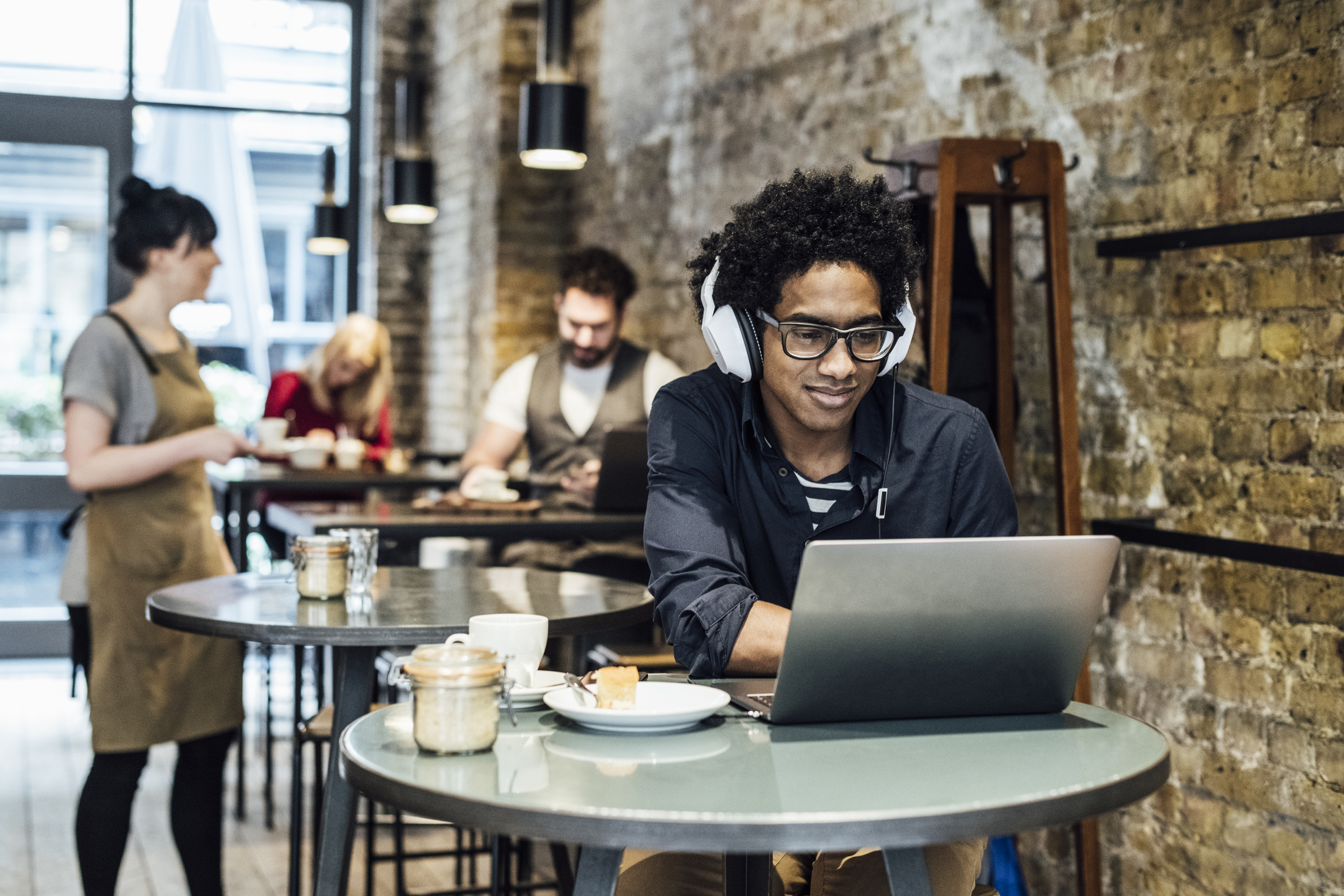 Person wearing headphones working on laptop at cafe.