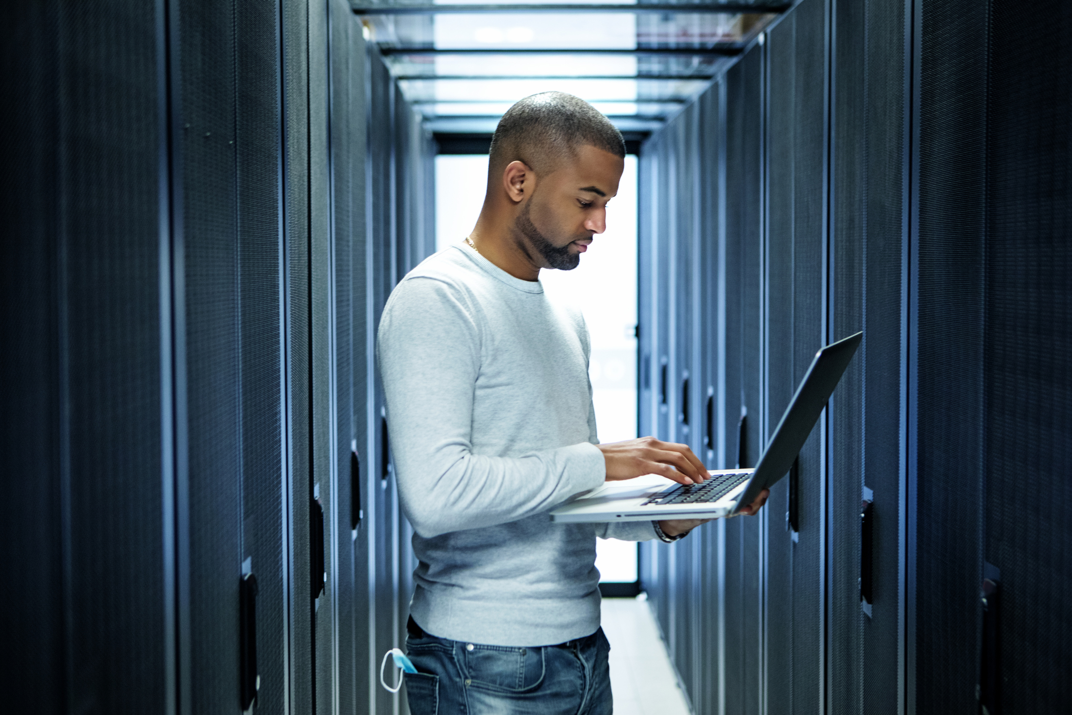 Worker checking laptop amid bank of servers.