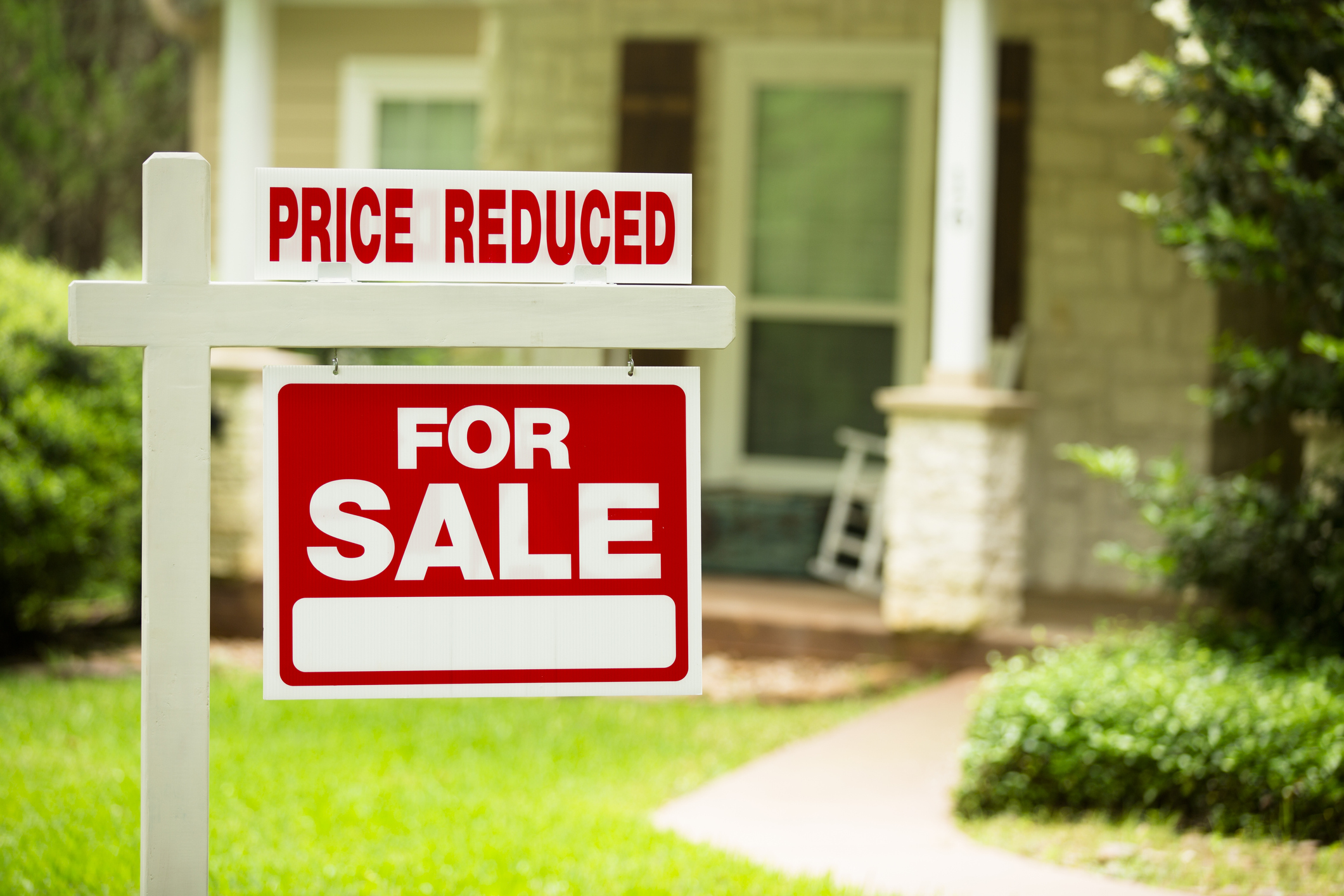 For-sale sign in front of home with words price reduced.