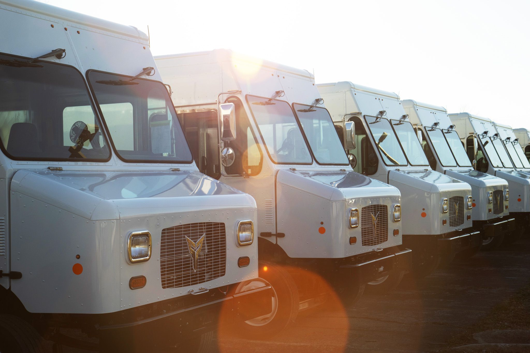 line of Xos electric delivery trucks in parking area.