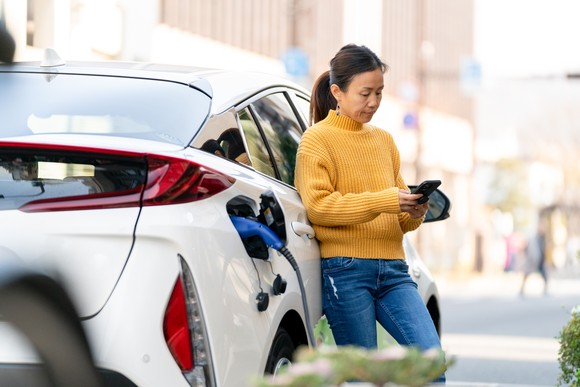 A person uses a cell phone while charging their electric vehicle.
