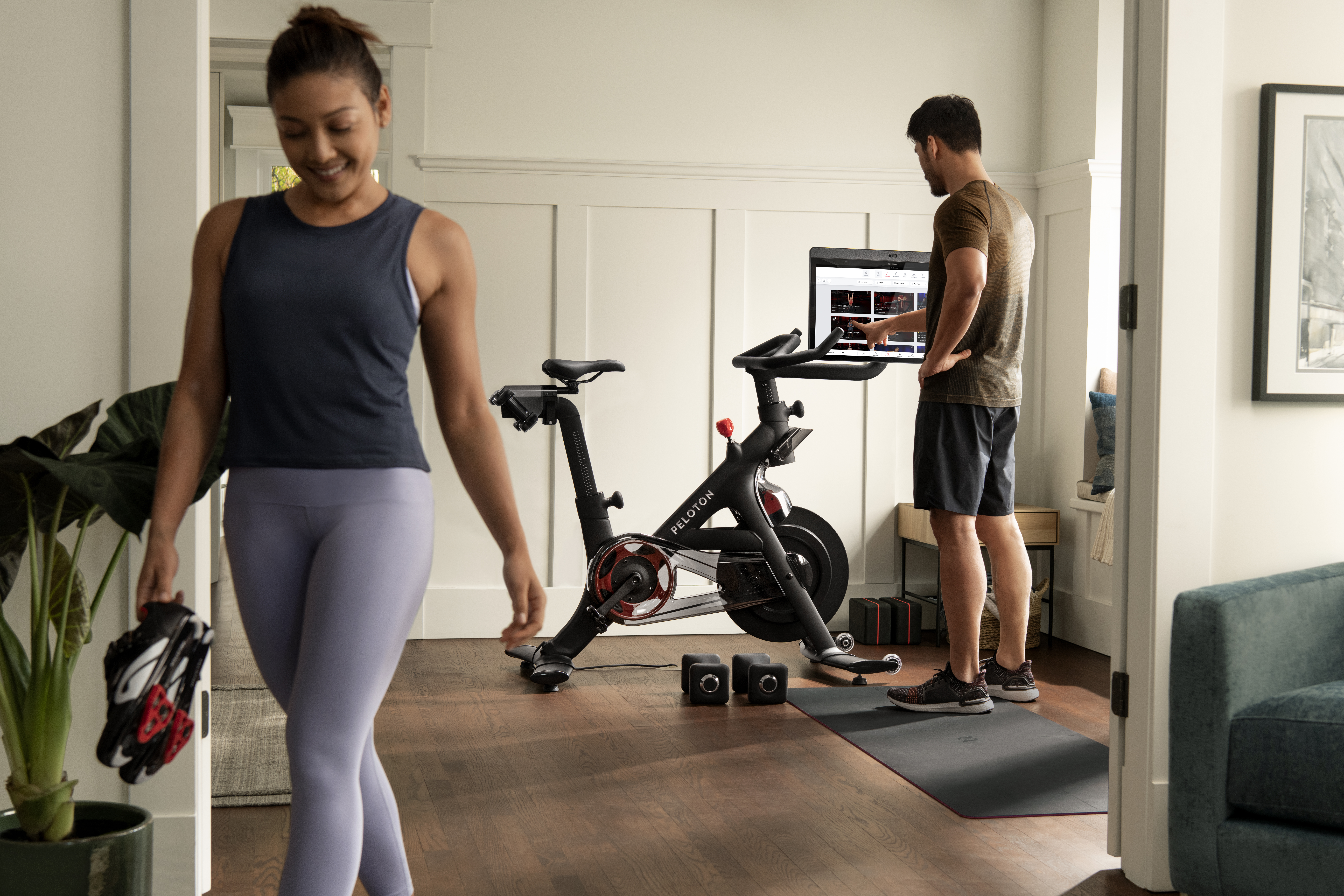 Two people dressed in workout clothes, in a room with a Peloton bike.