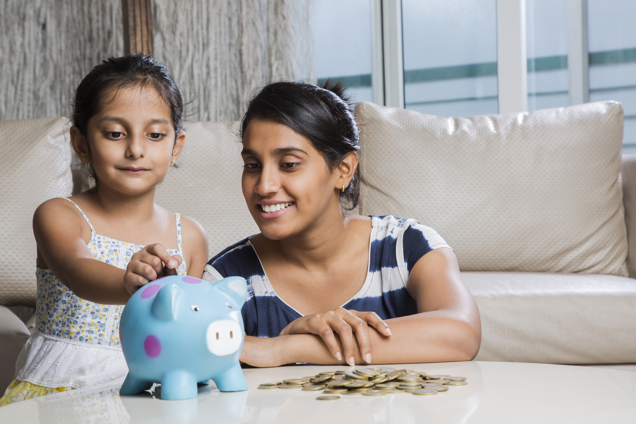 A person and a child putting coins in a piggy bank.