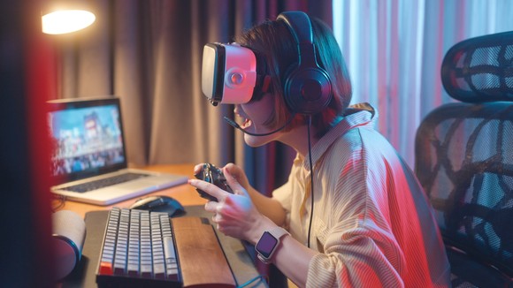 Person sitting on a desk wearing a headset and holding a controller.