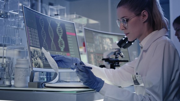 A scientist works on a computer showing DNA images.