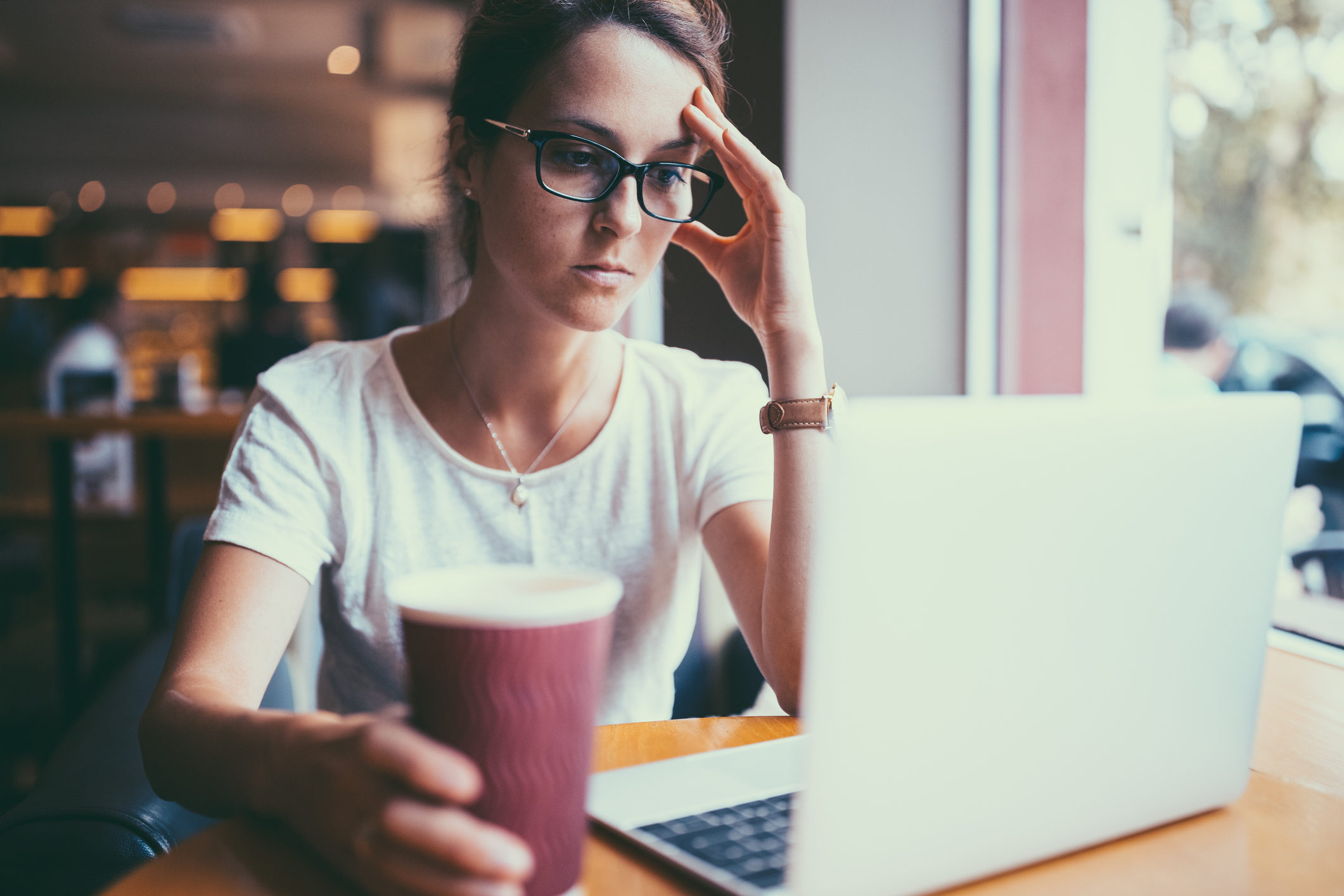 investor looking at laptop with cup of coffee and hand on head signaling despair.
