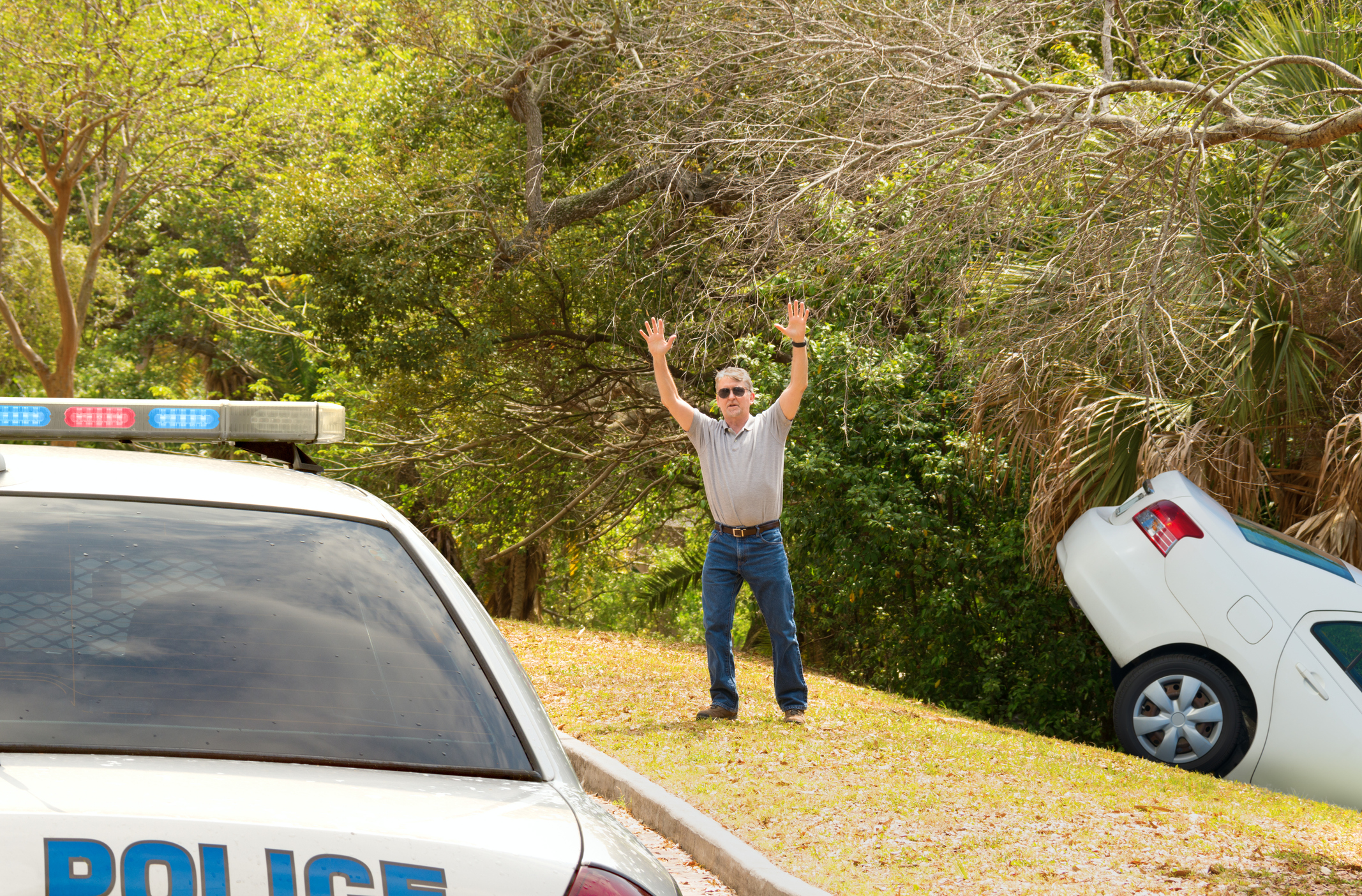 A person waves down a police car next to a car wreck in a ditch.