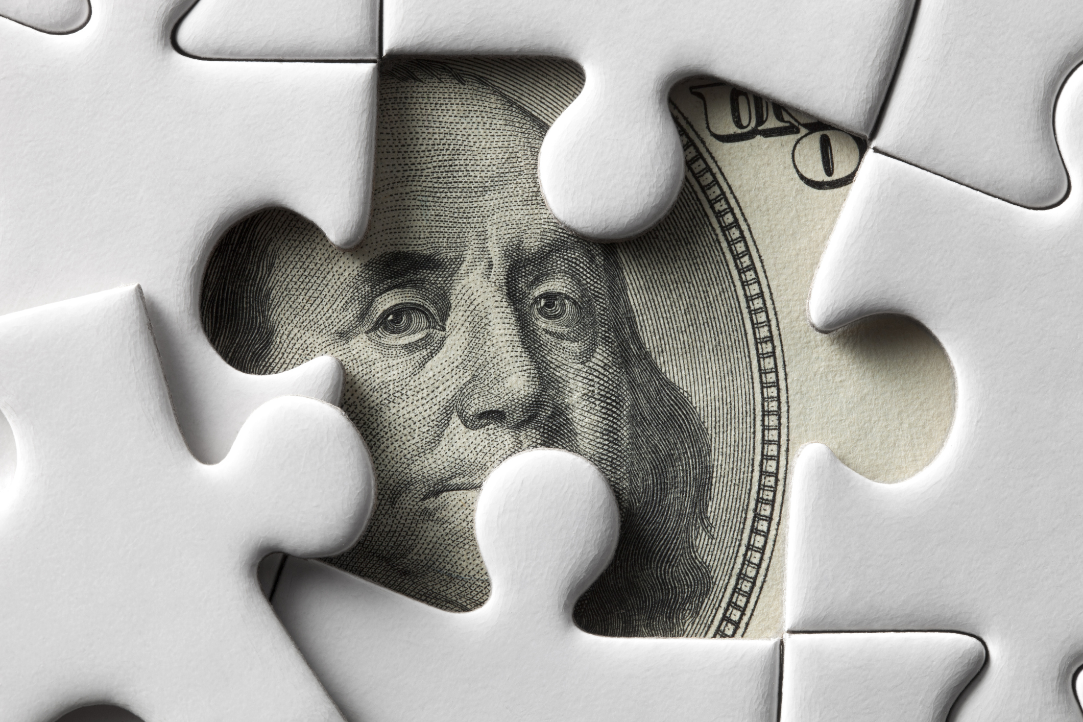 A hundred-dollar bill under a puzzle with a missing piece.