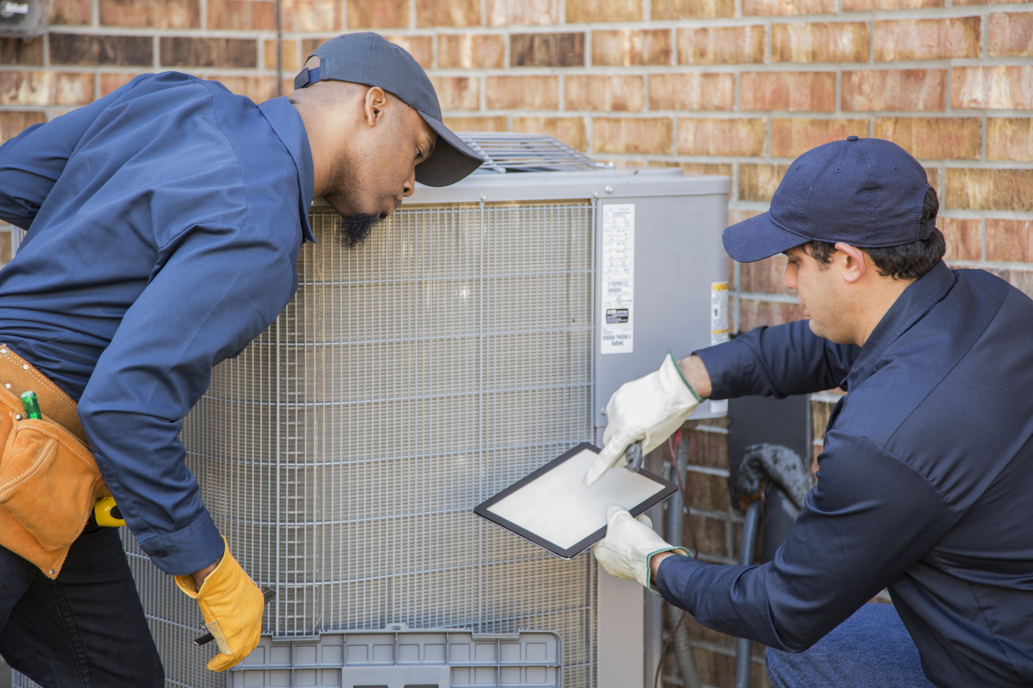 Two air conditioning repair people check a filter on an HVAC unit.