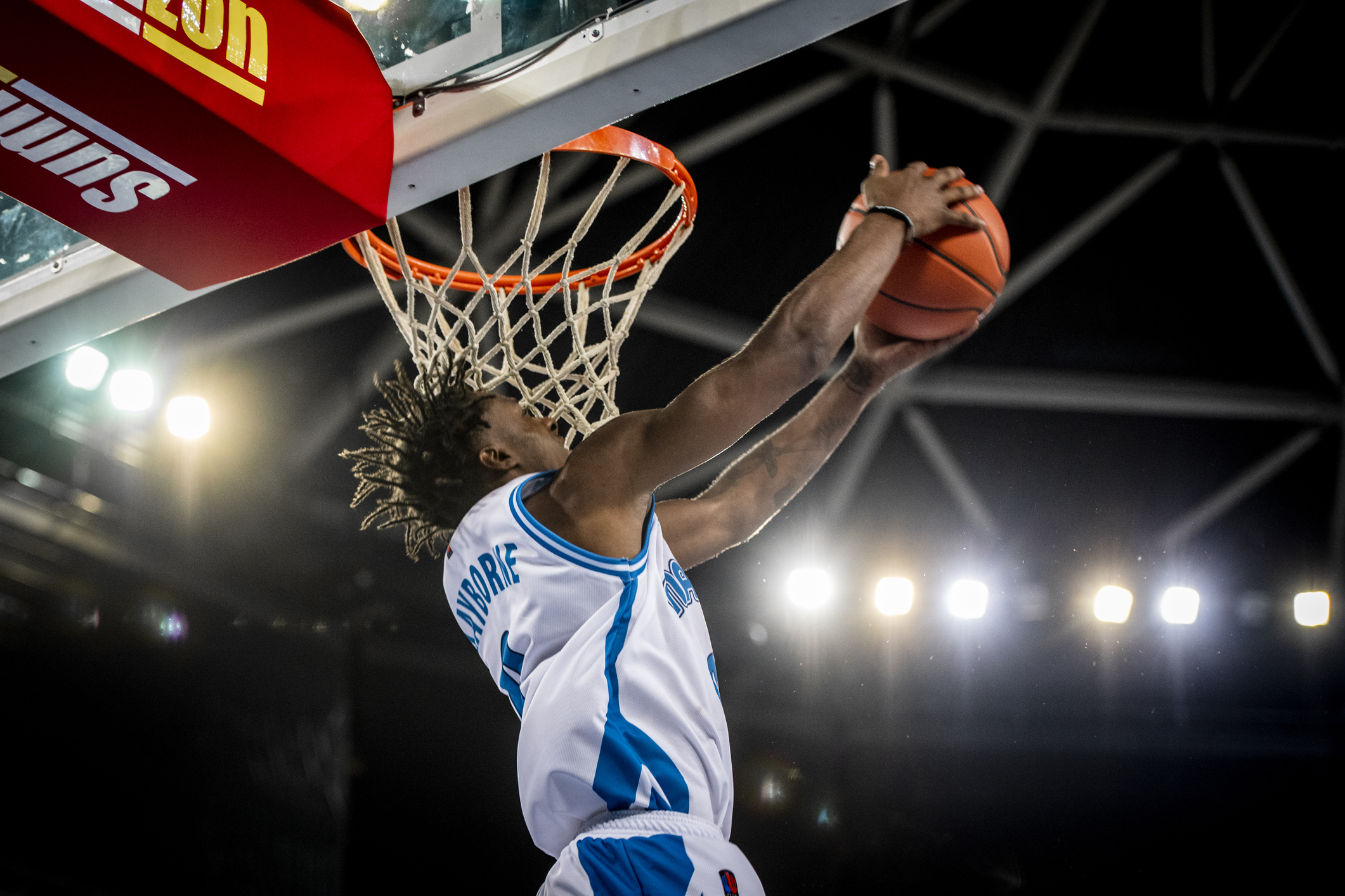 A player does a reverse dunk into a basketball hoop.